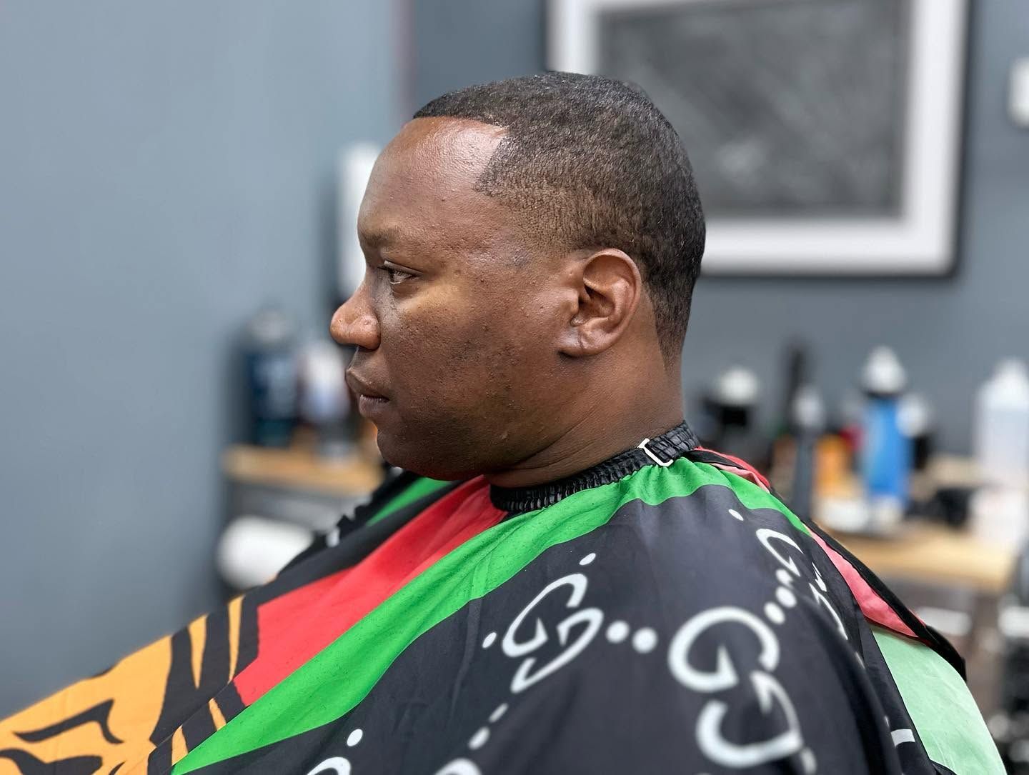 Man seated in a barber chair wearing a black, red, and green cape during a haircut