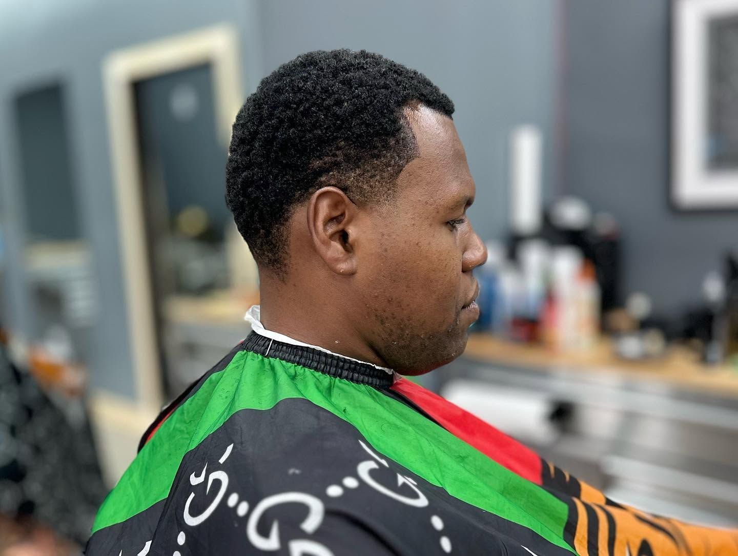 Person in a barber chair wearing a green haircut cape, side profile, in a salon.