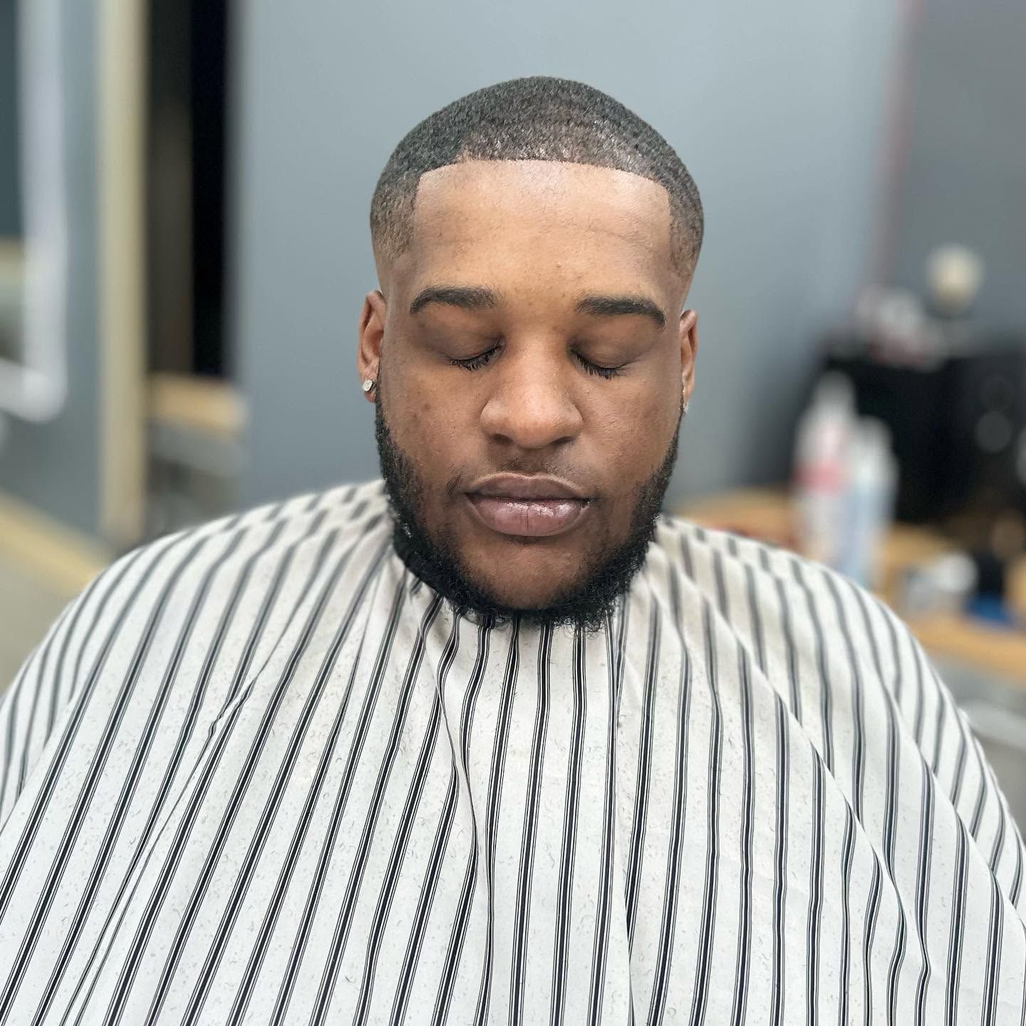 Man with eyes closed wearing a striped barber cape in a salon chair
