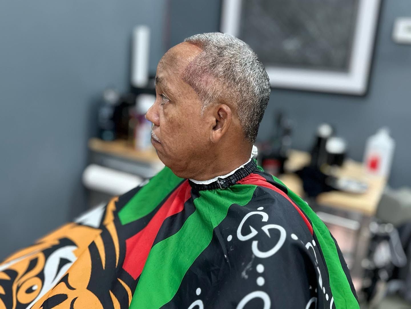 Man in a barber chair wearing a green, red, and black cape in a salon
