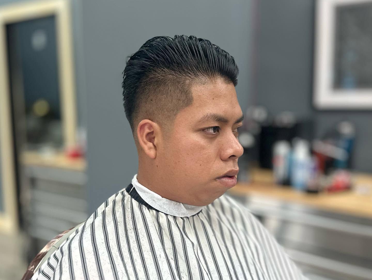 Man in a striped barber cape, side profile in a barbershop chair.