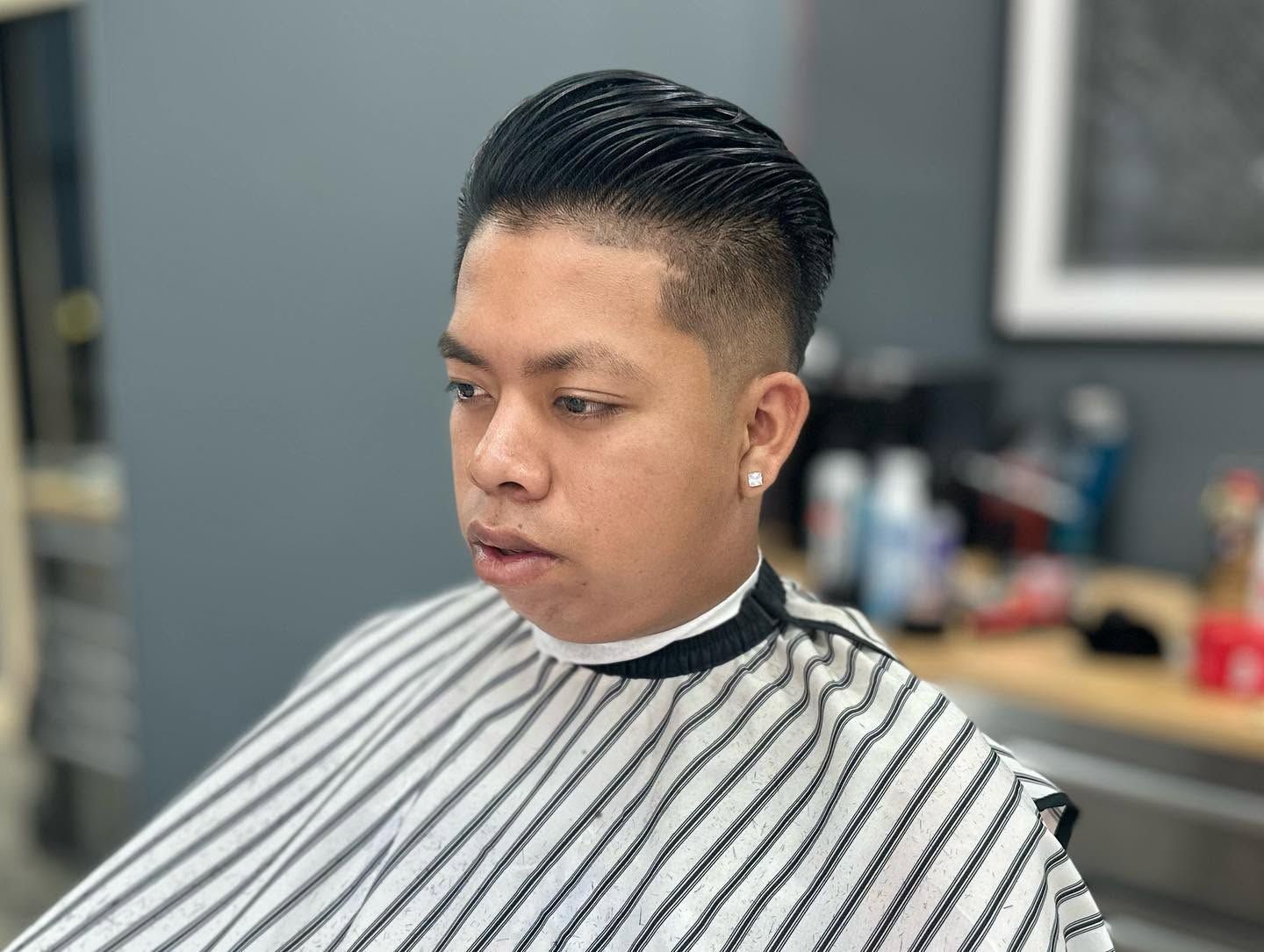 Person in a striped barber cape getting a haircut in a barbershop.
