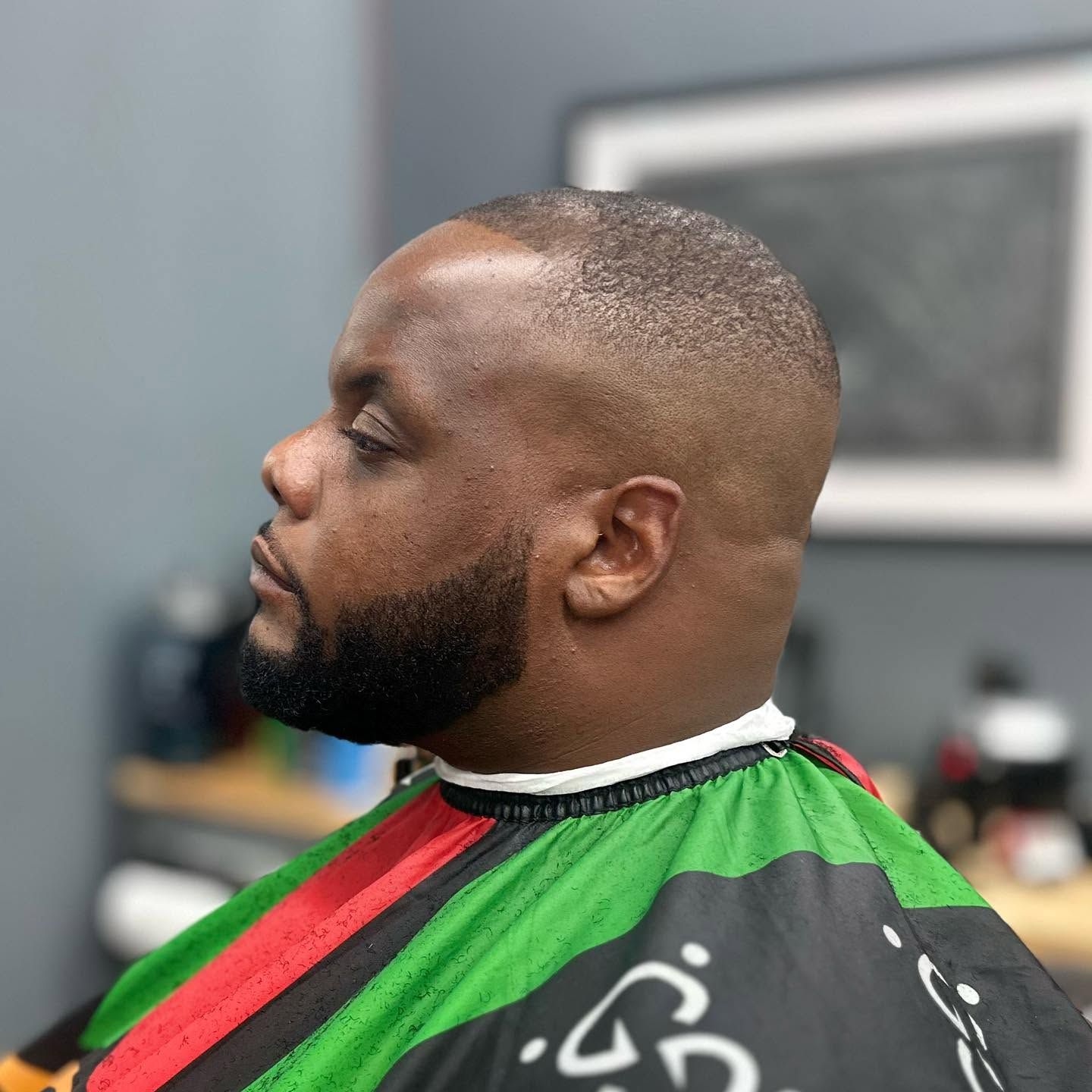 Side profile of a man with a fresh fade haircut wearing a black, green, and red barber cape.