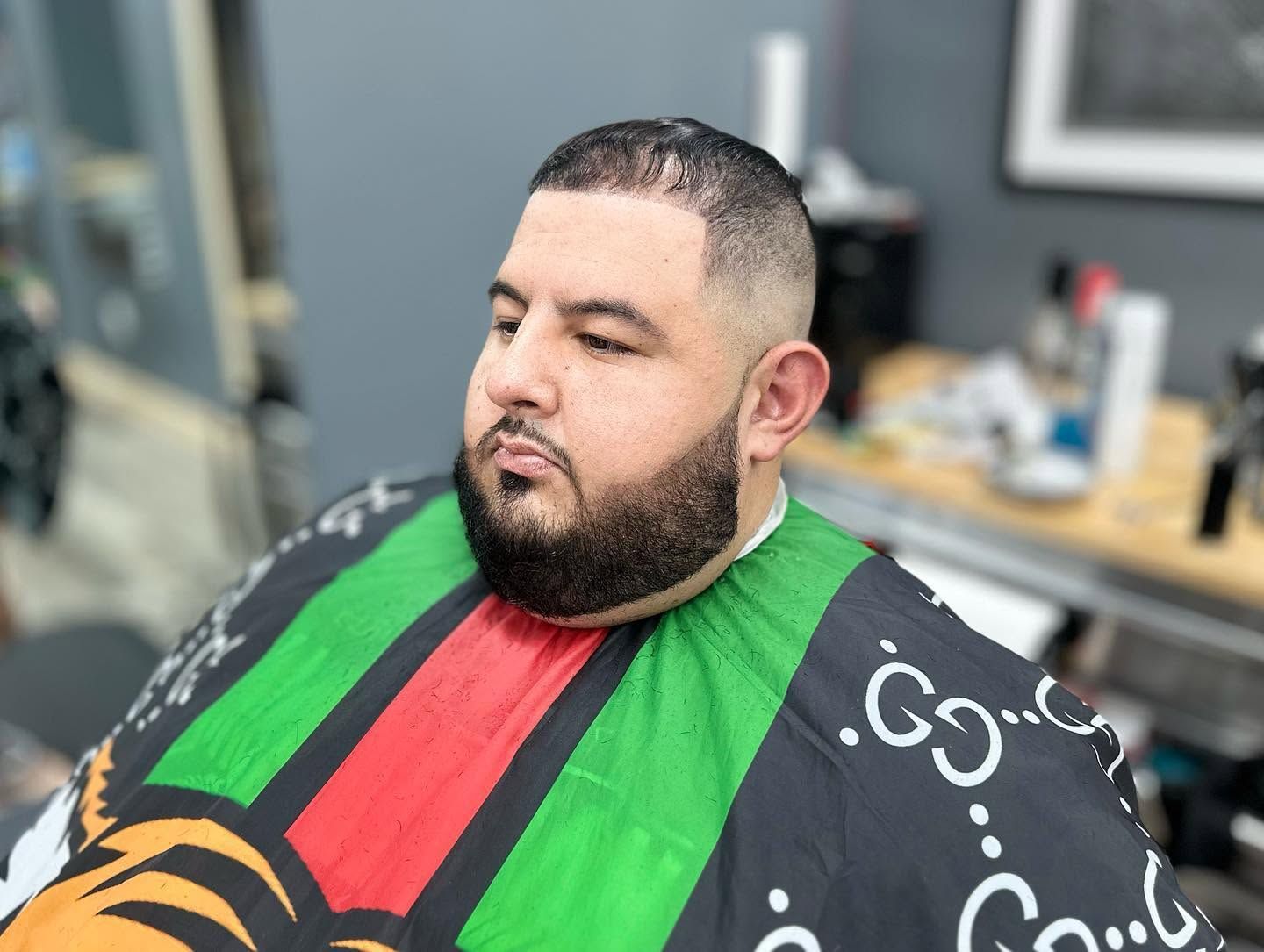 Man seated in a barber chair with a fresh haircut and beard, wearing a colorful barber cape.