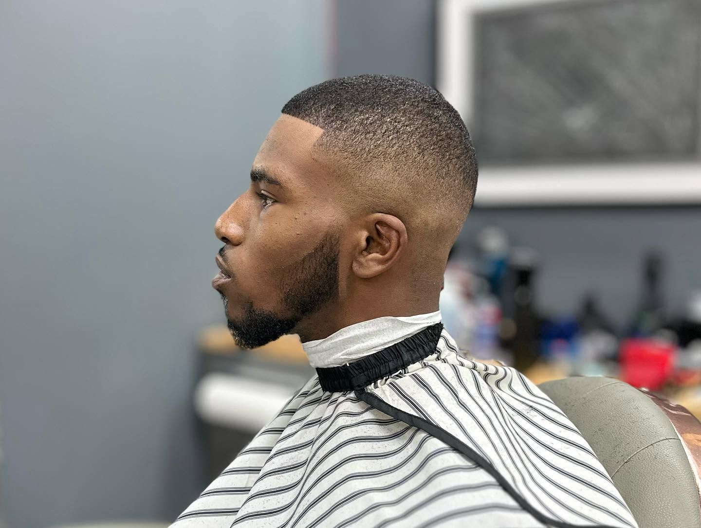 Man with a close fade haircut sitting in a barber chair, wearing a striped cape during a haircut