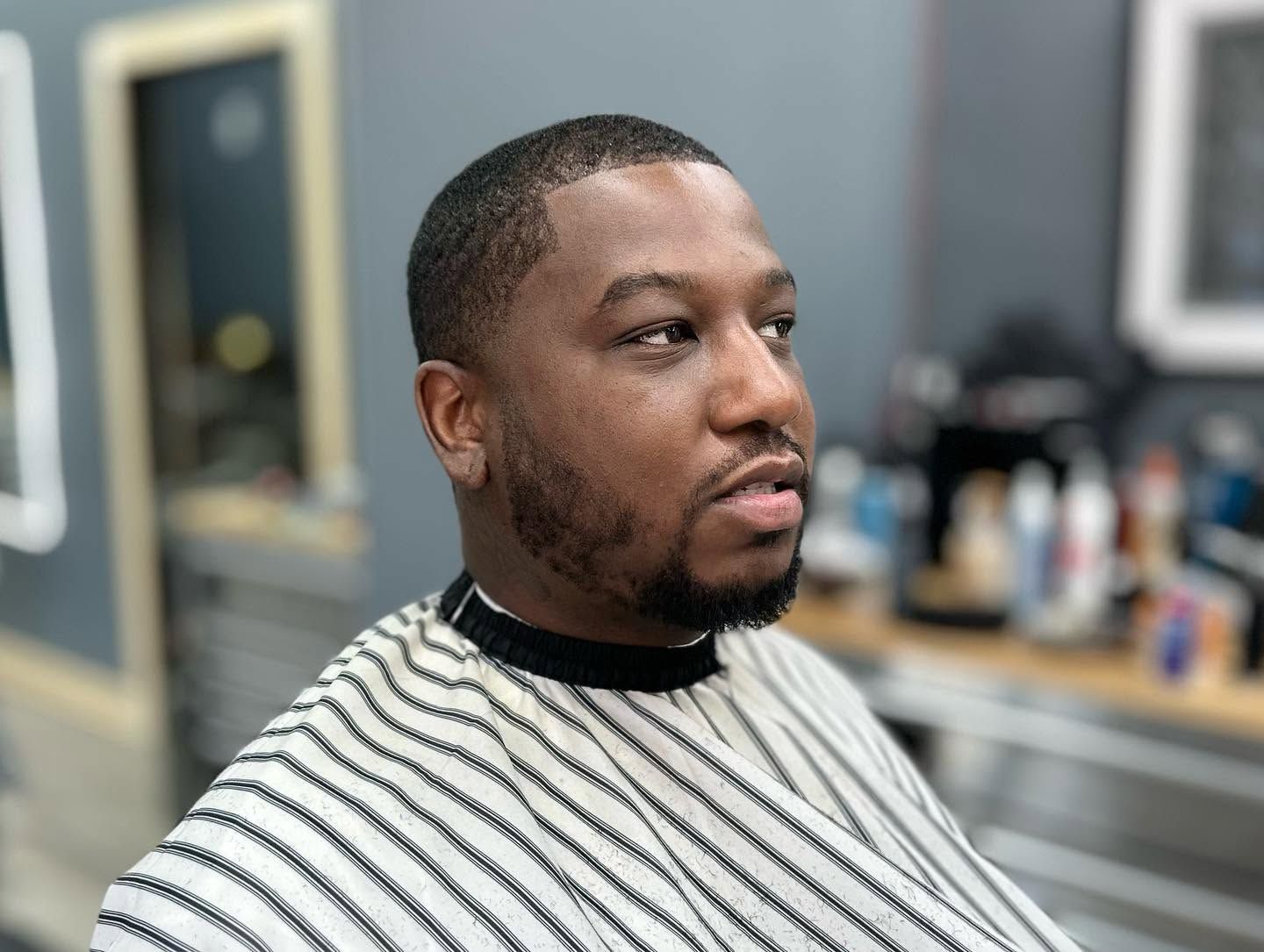 Man in striped barber cape getting a haircut in a salon, with a mirror and grooming tools in the background