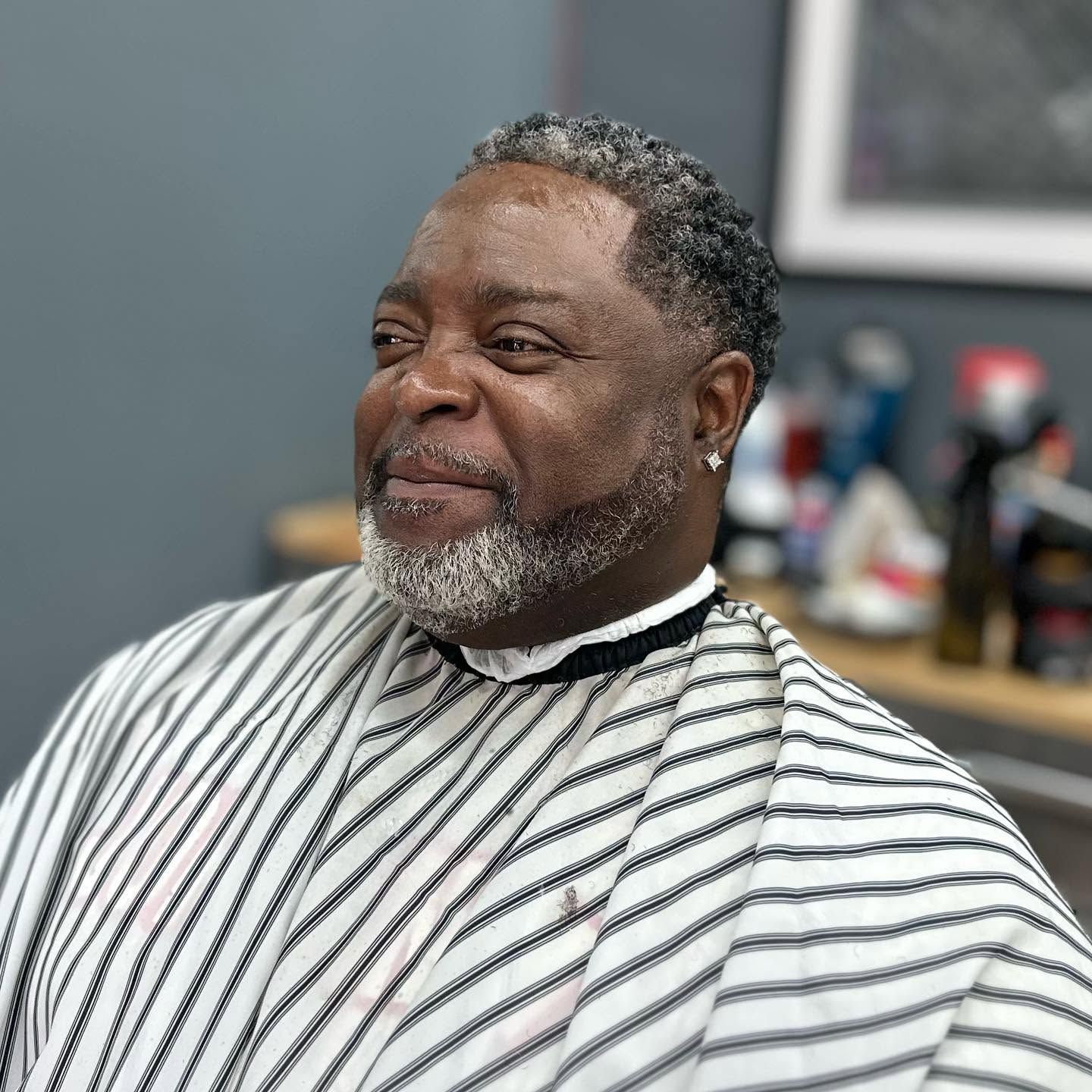 Man in a black-and-white striped barber cape, smiling in a barbershop chair