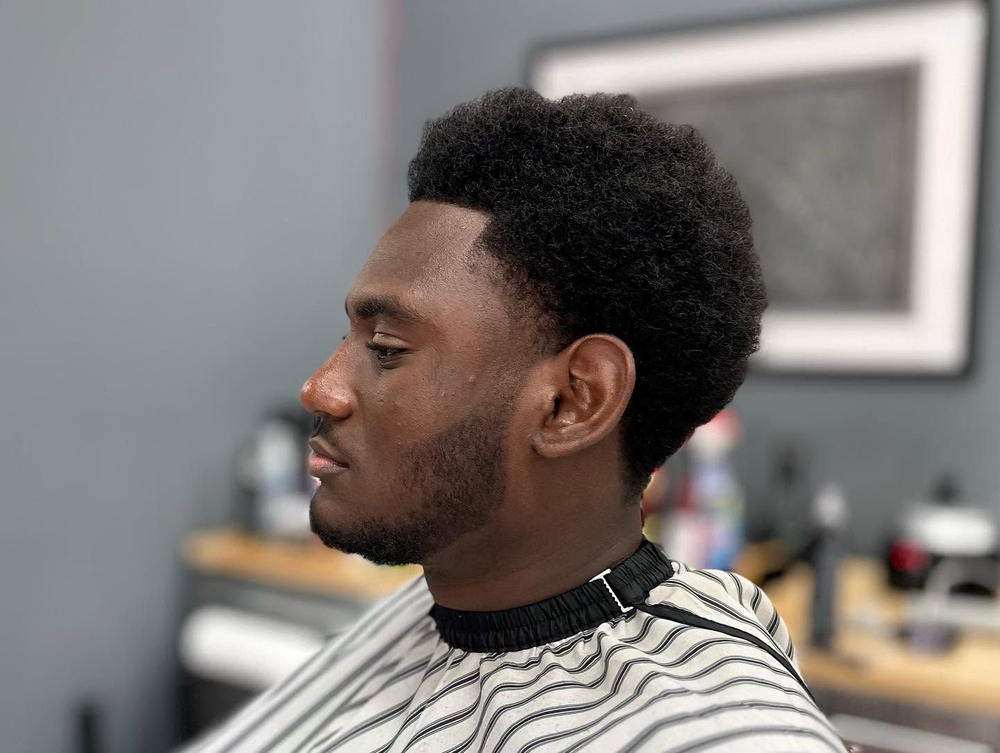 Profile view of a man with a short afro in a barber chair, wearing a striped cape