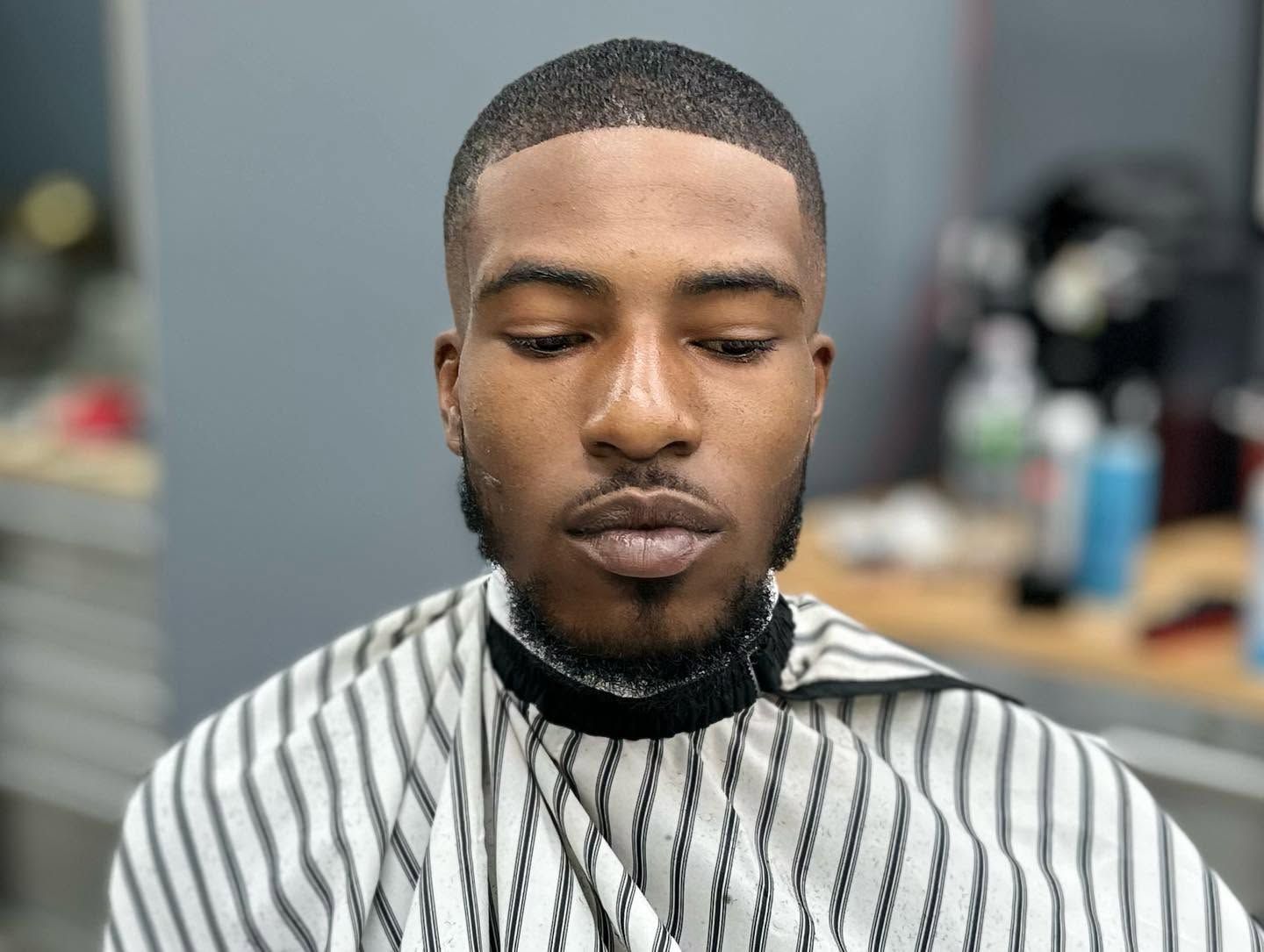 Portrait of a man with a striped barber cape in a barbershop, looking down