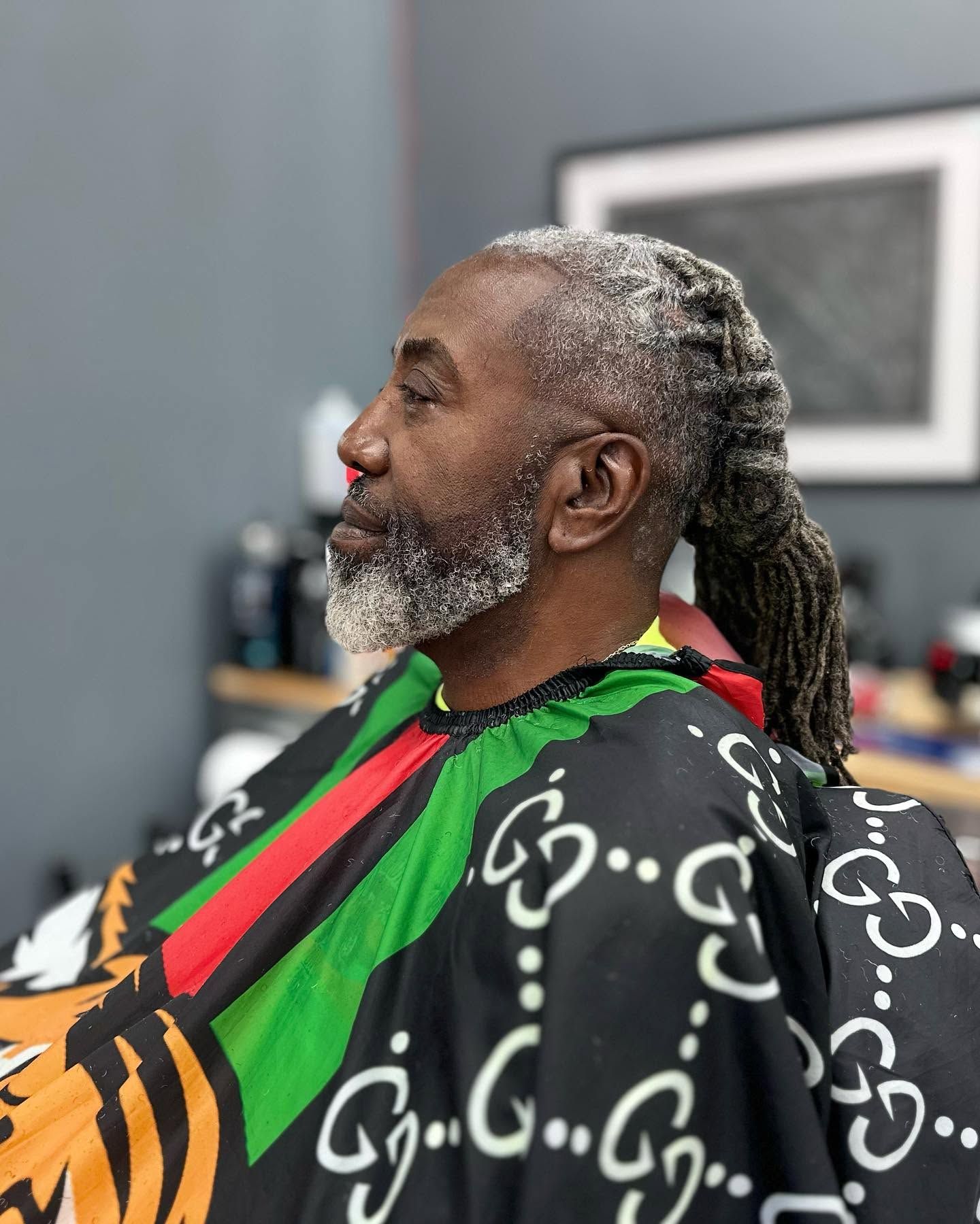 Profile of a man with gray beard and ponytail wearing a colorful barber cape in a salon