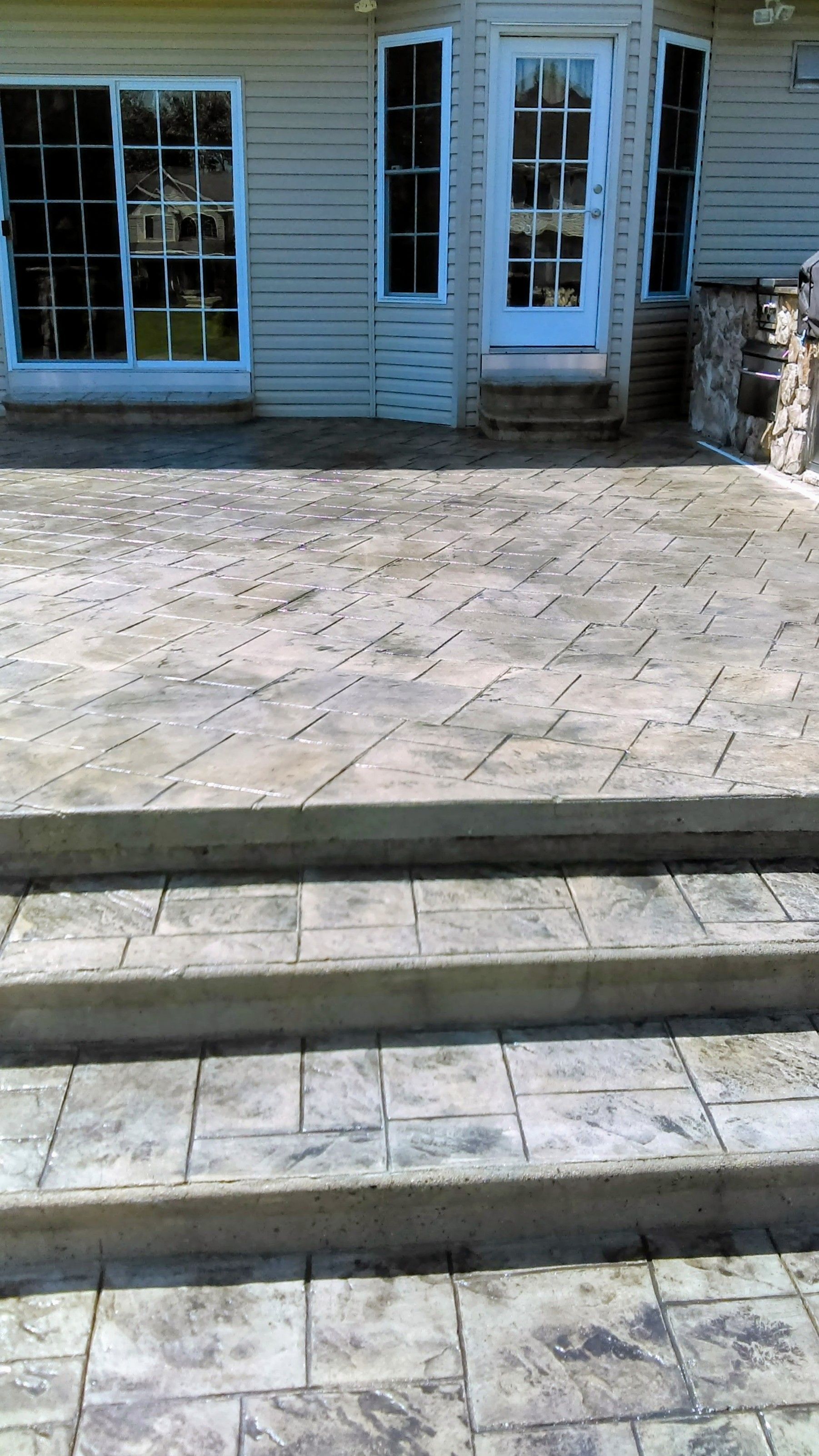 Concrete patio with steps leading to a house with windows and a white door.