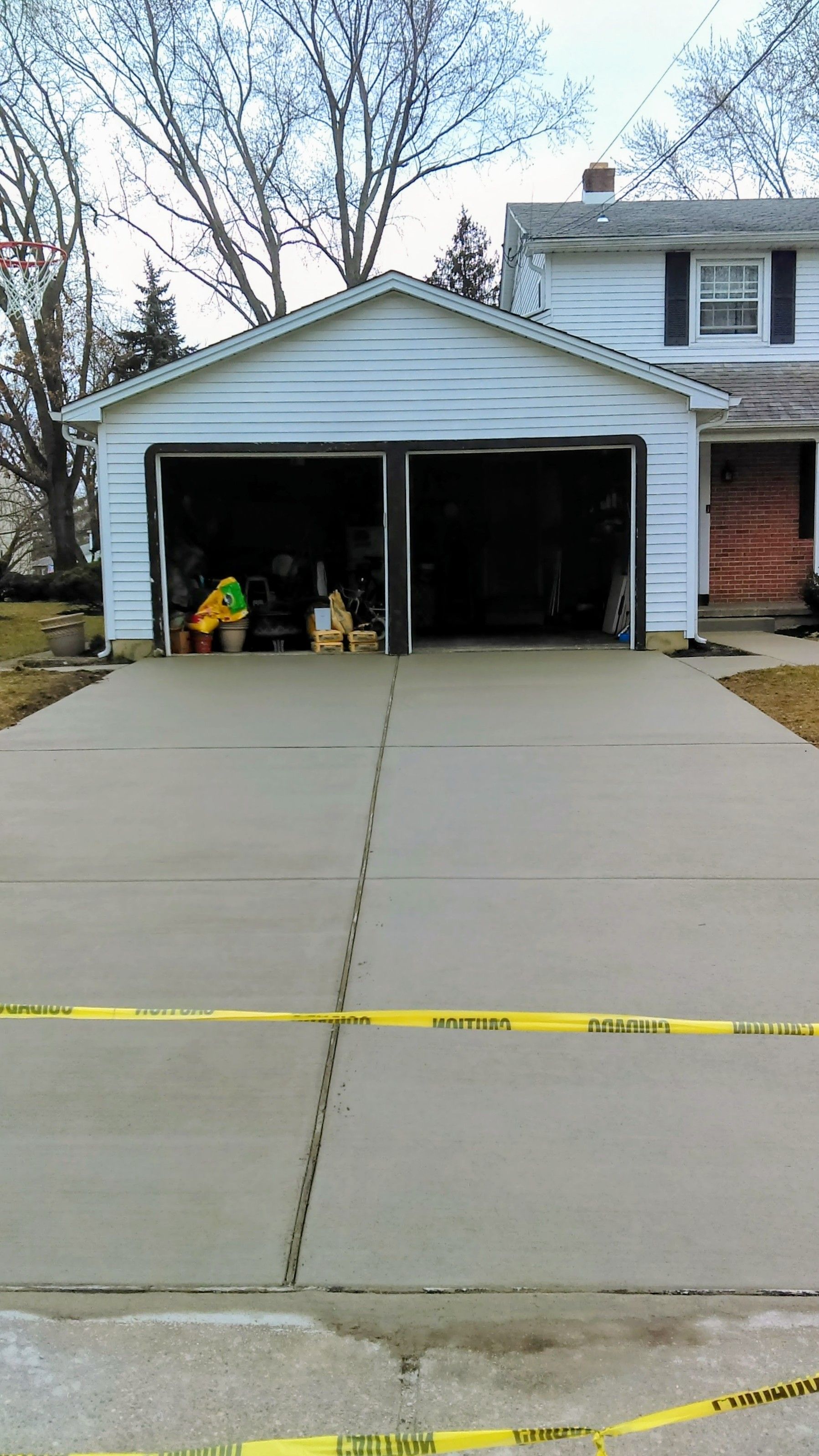 Garage with damaged door, open, yellow caution tape in front. Concrete driveway in foreground.