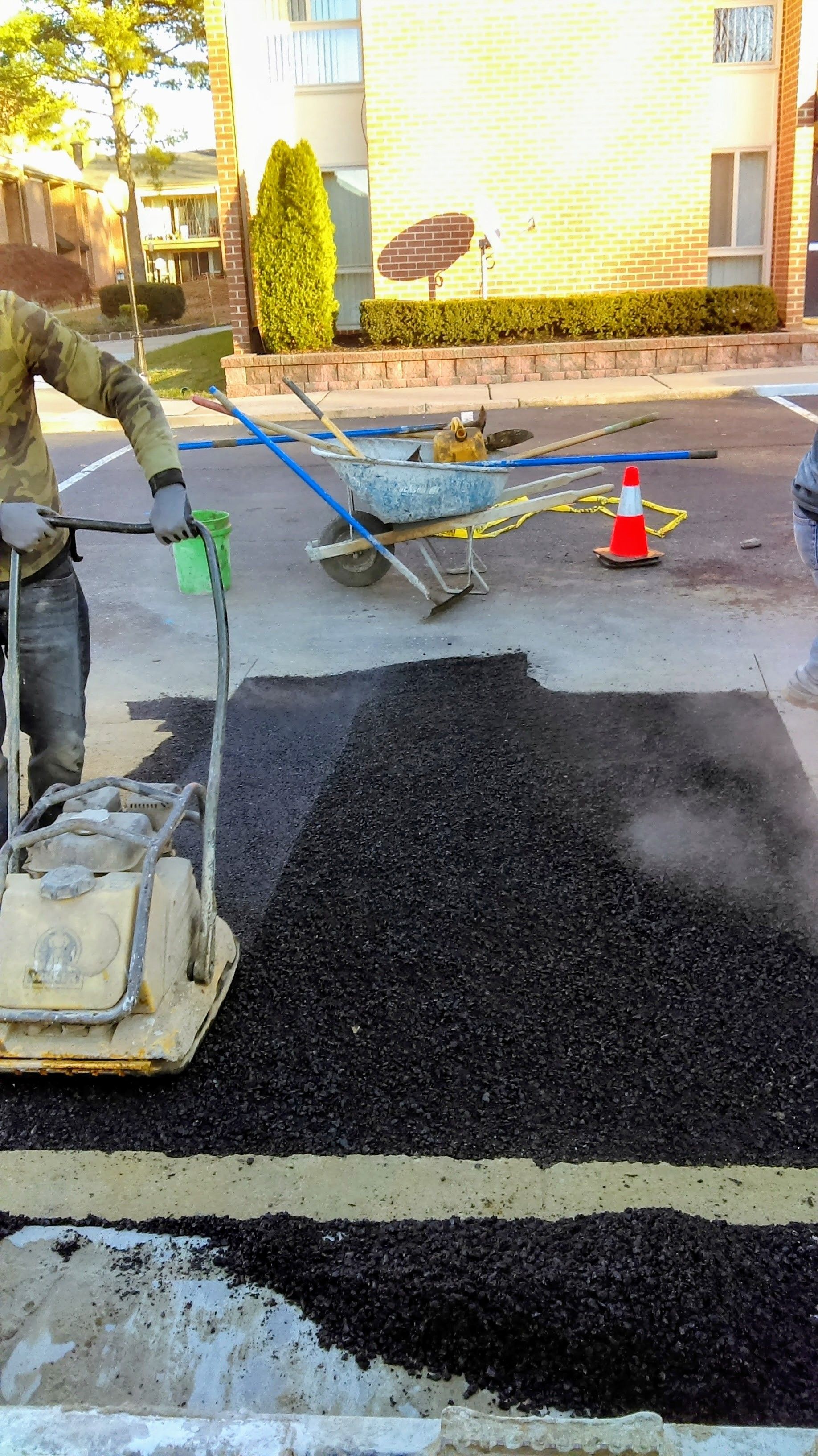 Person operating a vibratory plate compactor on asphalt. Parking lot repair in progress.