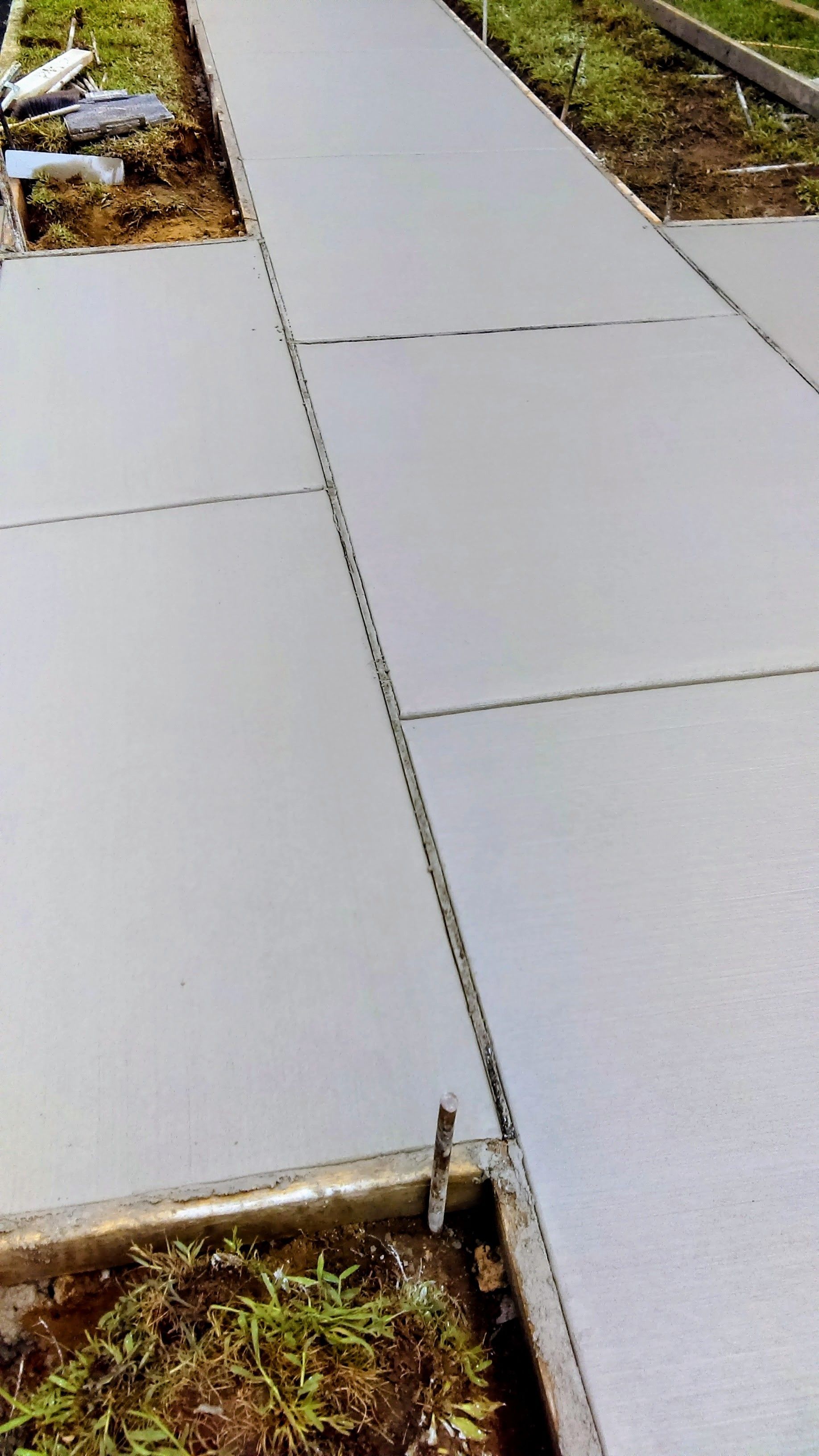 Newly poured concrete sidewalk with fresh, gray surfaces. Sections separated by joints.