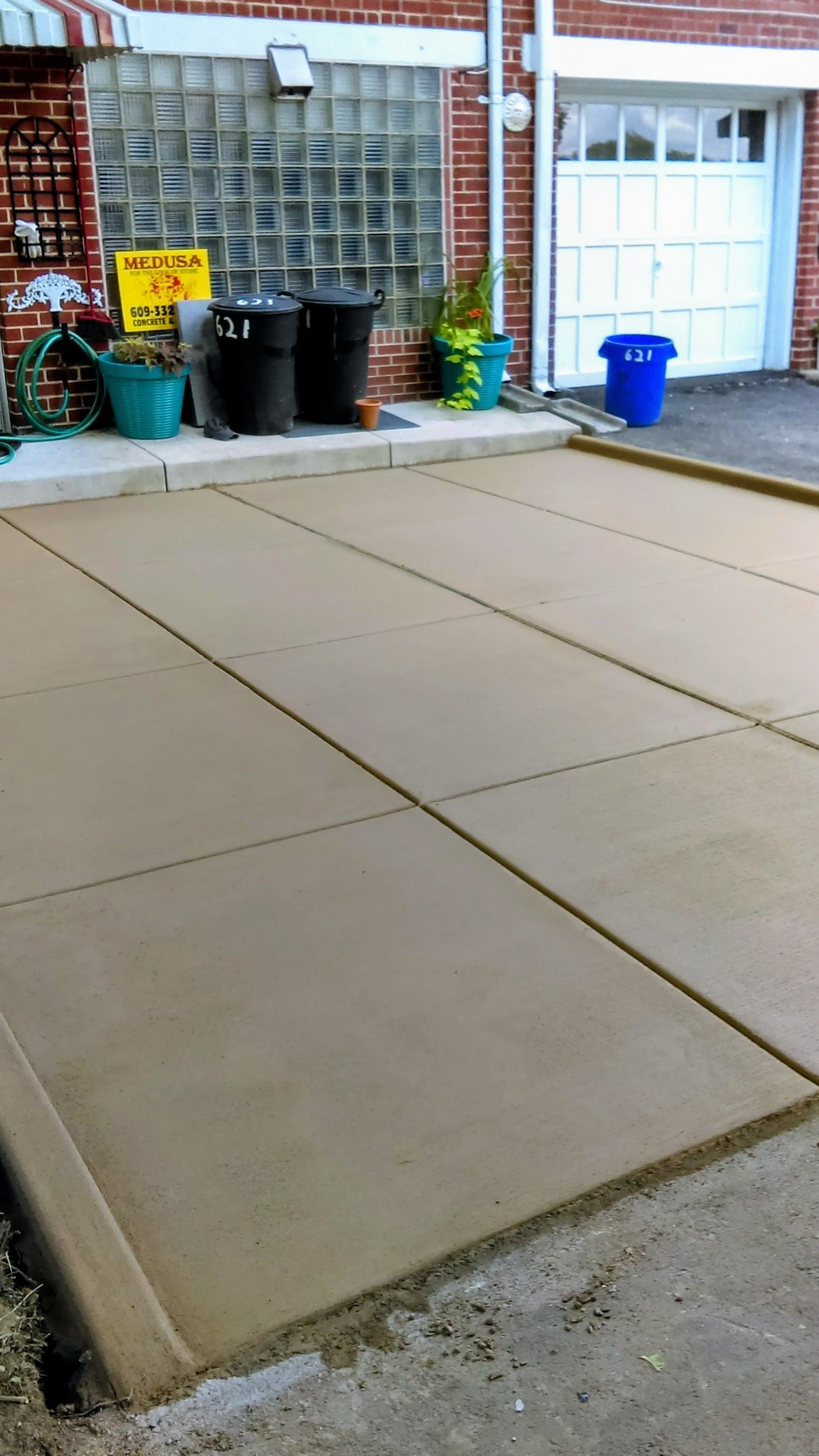 Newly poured concrete driveway in front of a brick building with a garage door.