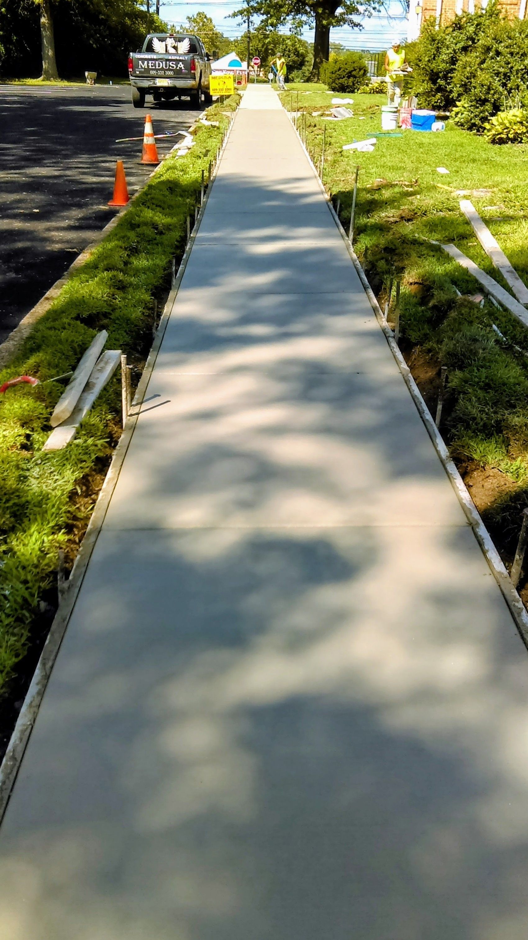 Newly poured concrete sidewalk with wood forms on either side, bordered by grass and a street.