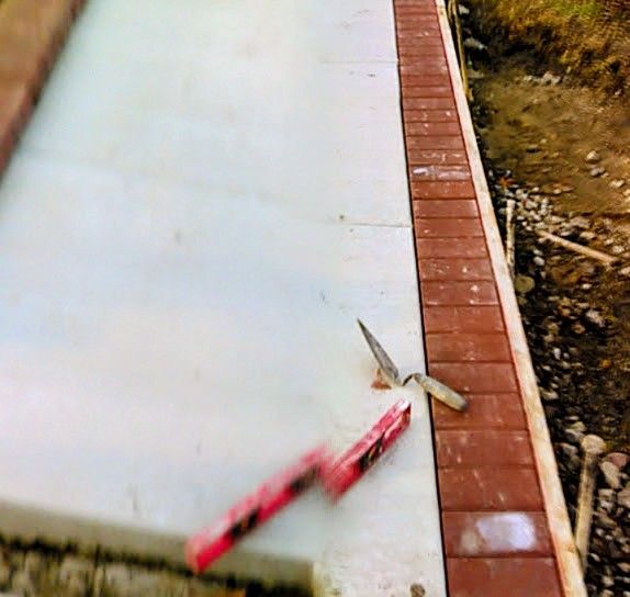 Construction site: Concrete slab with brick edging; trowel and level on the surface.