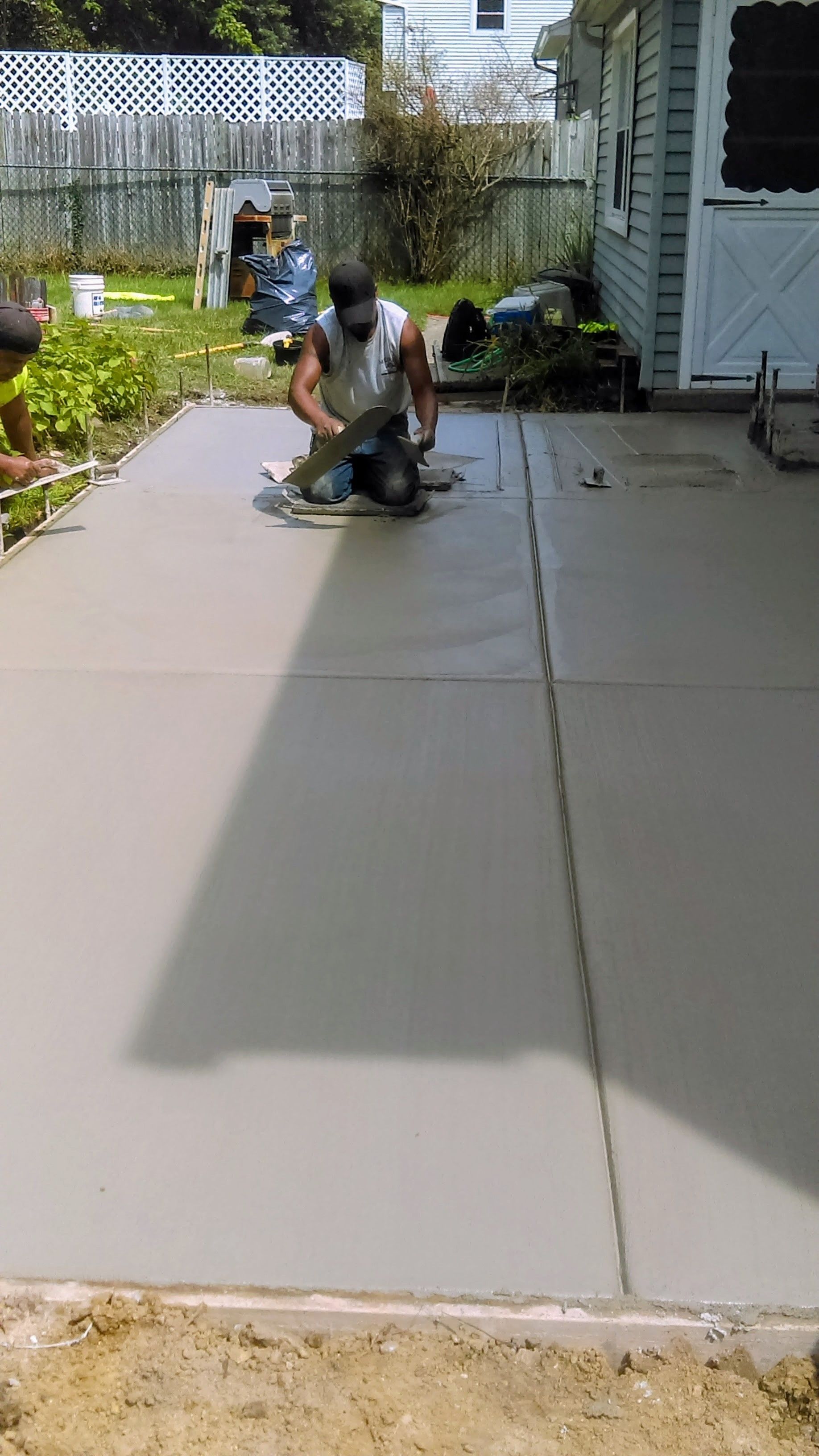 Workers finishing a concrete patio with power tools outdoors.