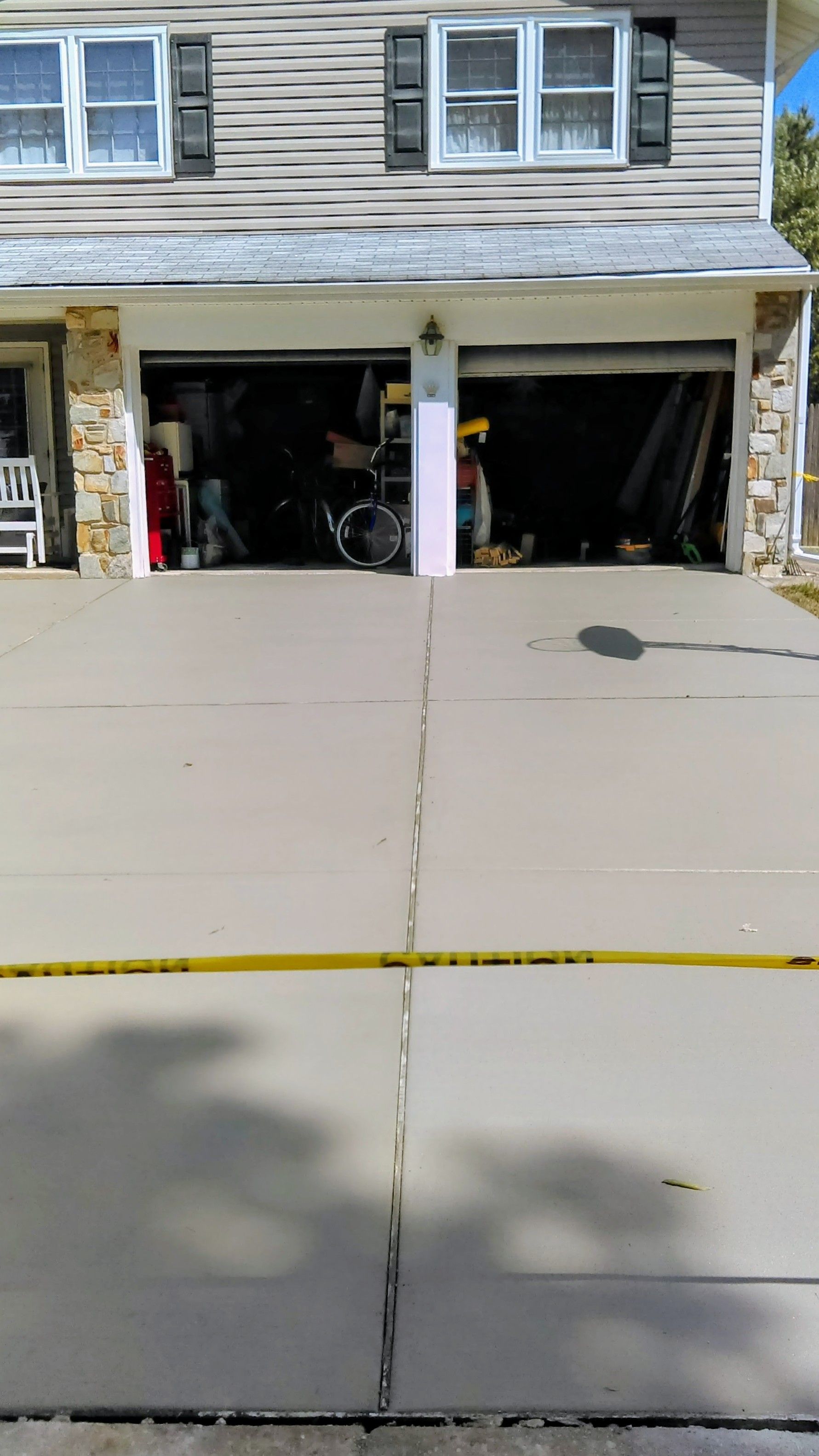 Two-story house with open garage doors; yellow caution tape across driveway. Garage is cluttered.