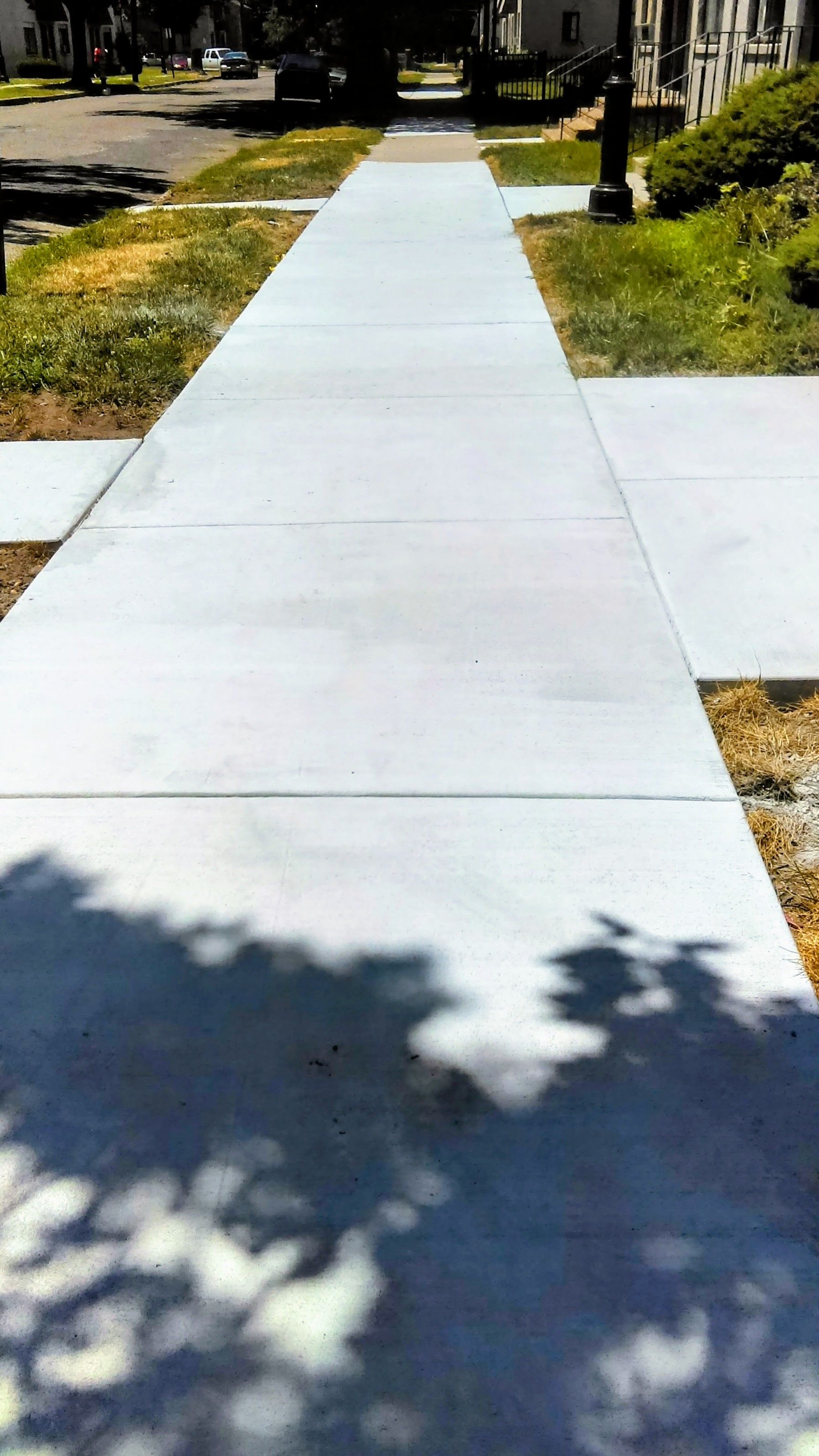 Concrete sidewalk extending down a residential street, with grassy areas on both sides.