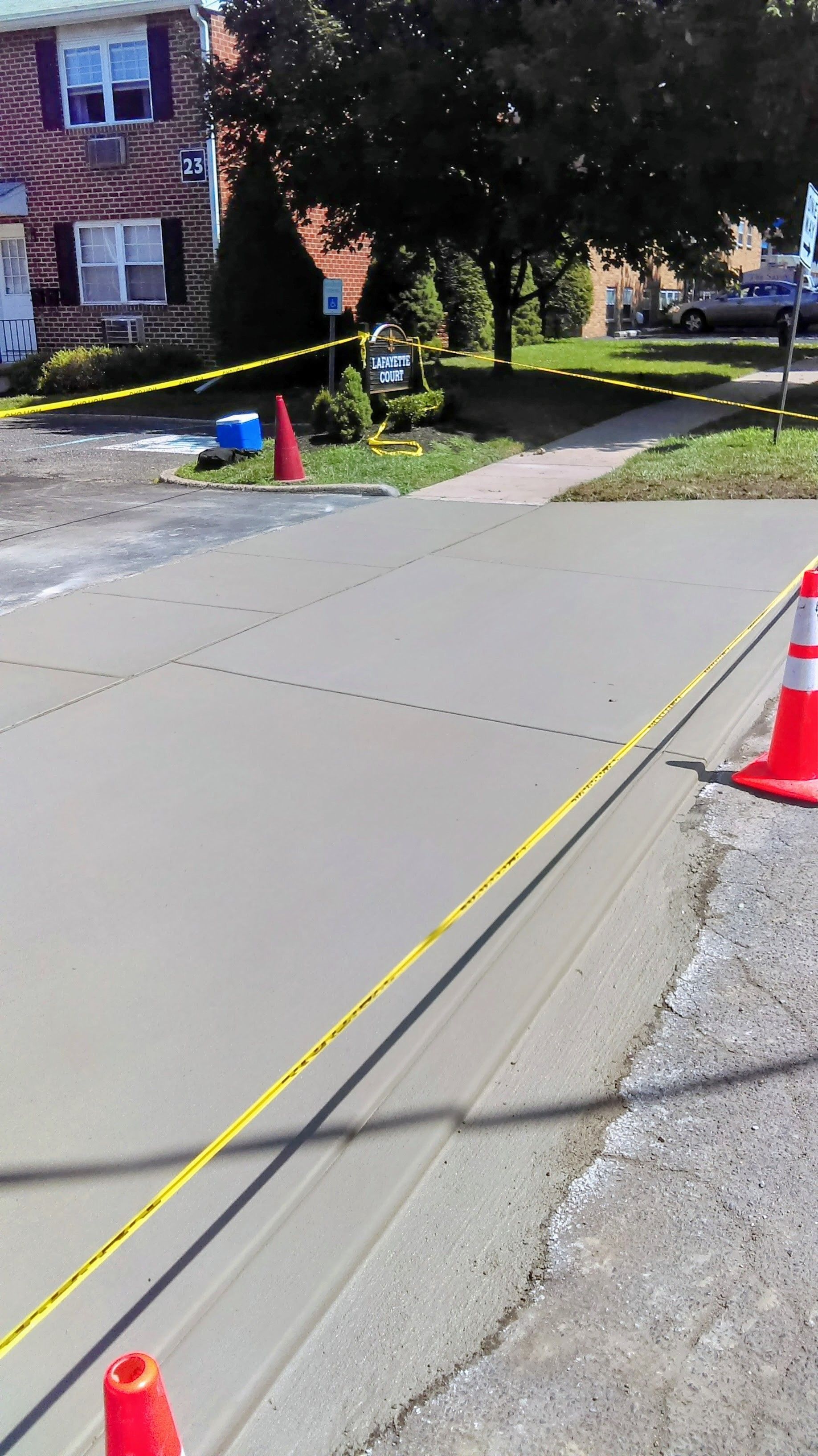 Newly poured concrete driveway, marked off with caution tape and traffic cones.