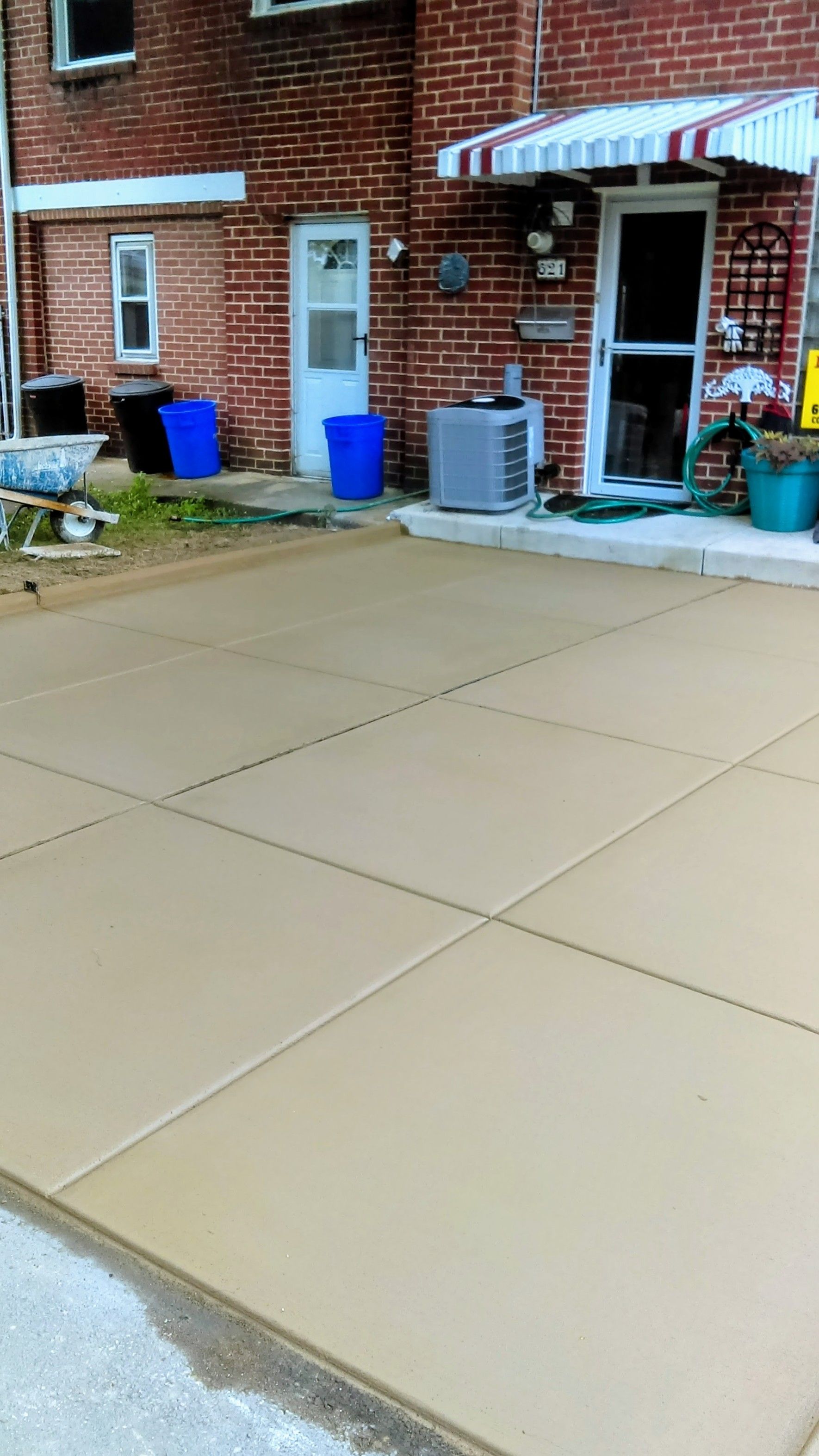 Newly poured concrete driveway in front of a brick building with doors, windows, and air conditioning unit.