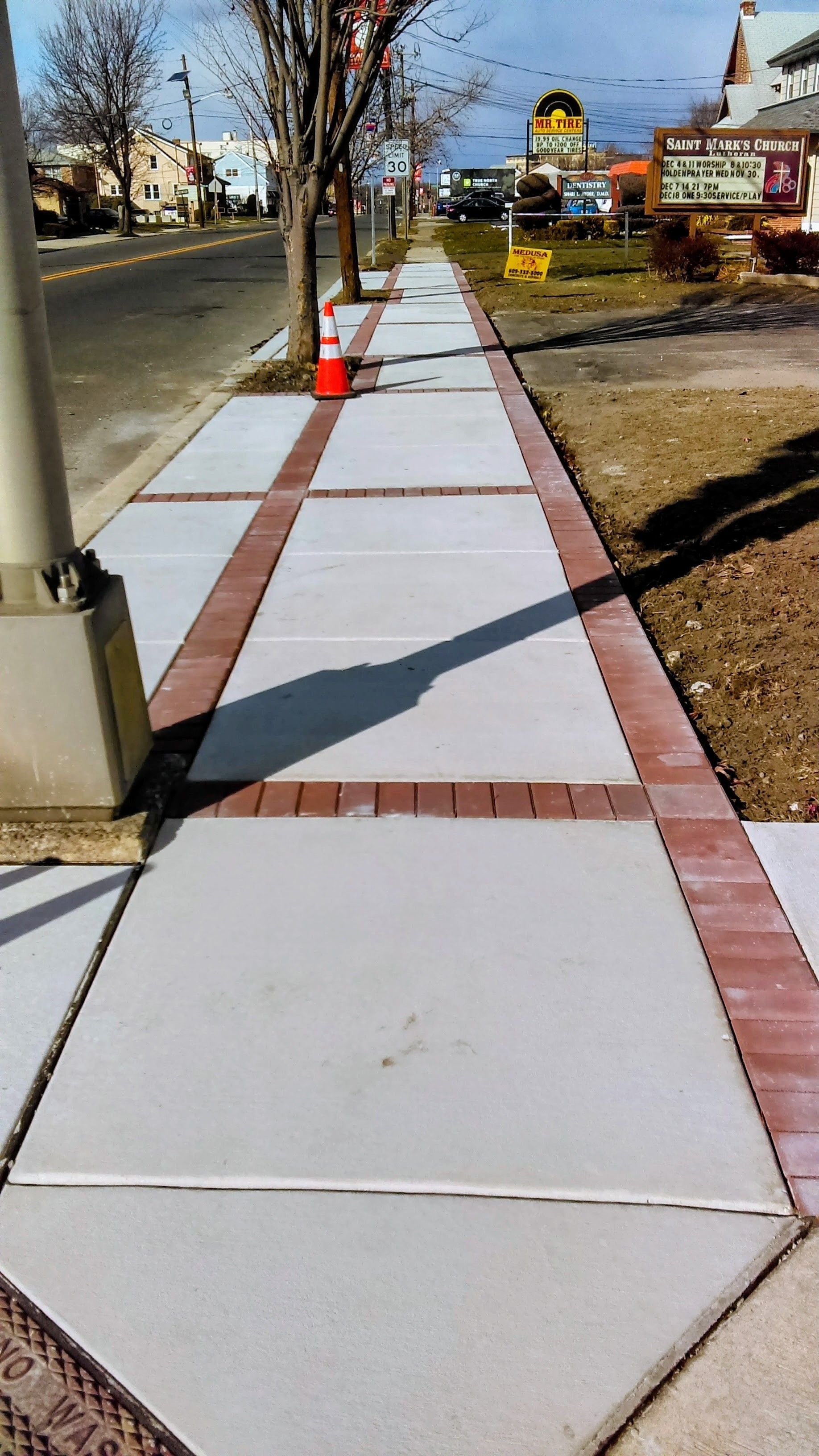 Sidewalk with gray concrete squares framed by brick, next to a street.