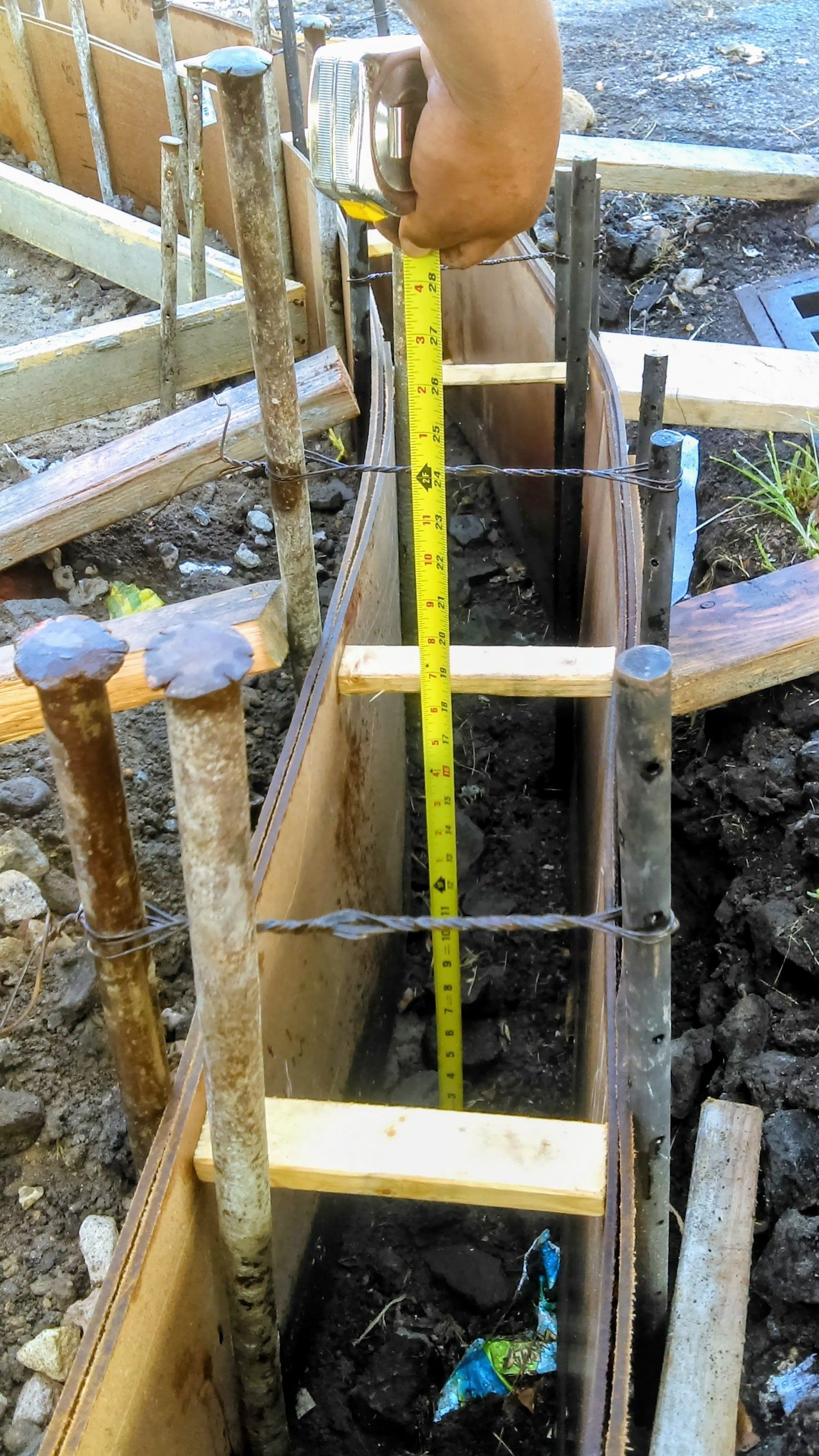 Person measuring a narrow trench with a yellow tape measure, likely for a concrete foundation.