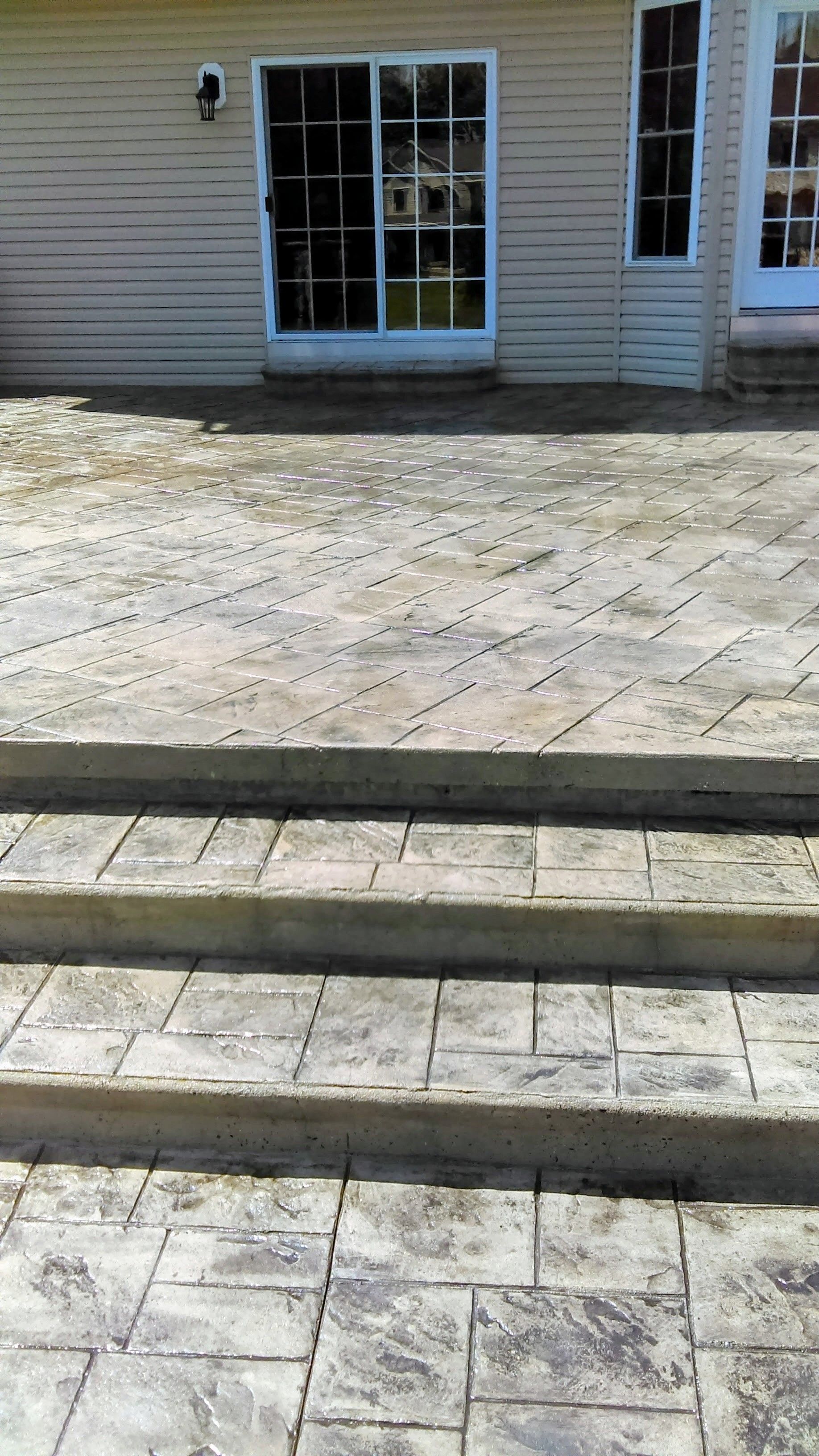 Gray concrete patio with steps leading down from a house with a sliding glass door.