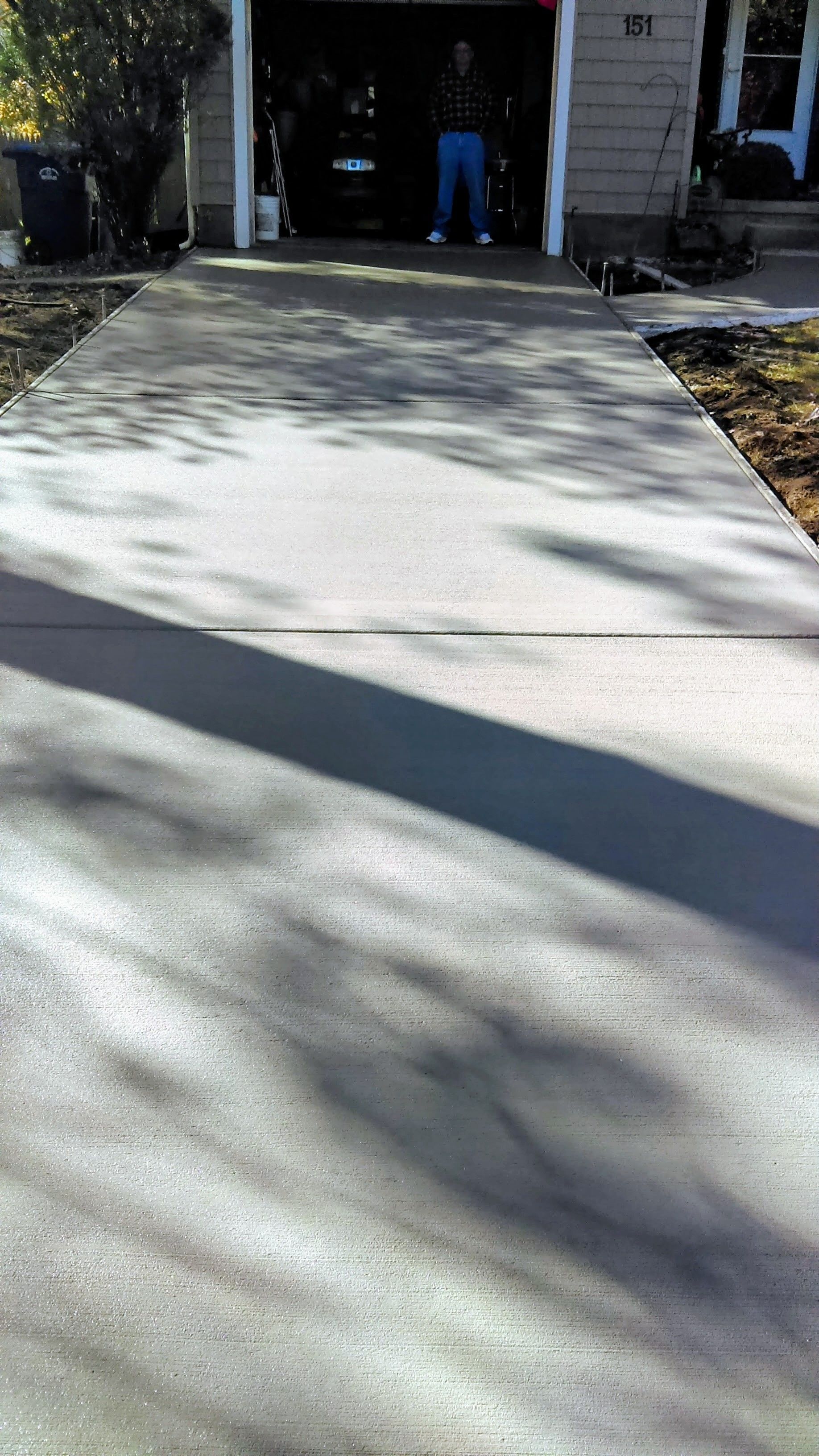Newly poured concrete driveway leading to a garage; a person stands inside the garage doorway.