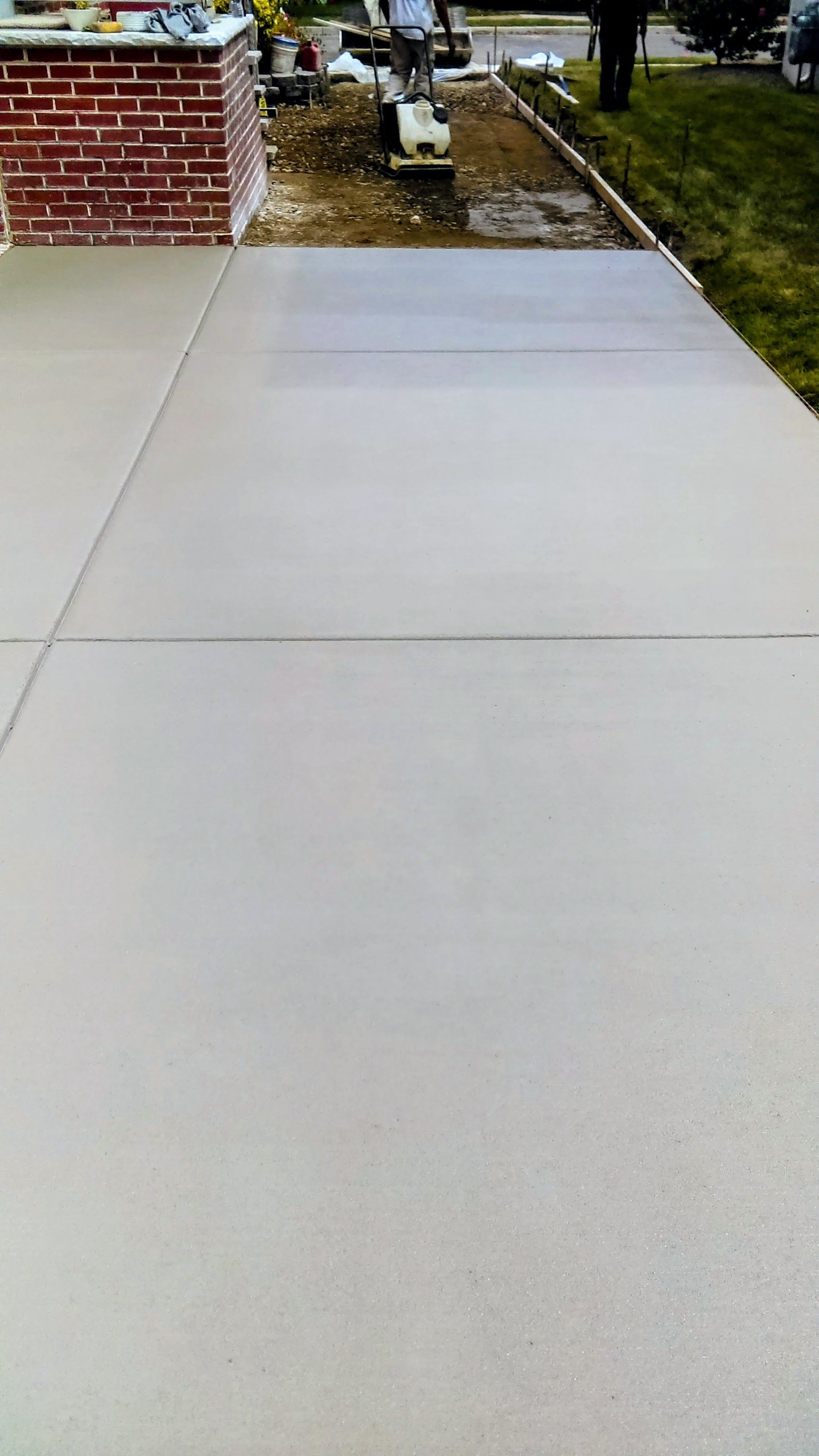 Newly poured concrete walkway next to a brick structure and grass.