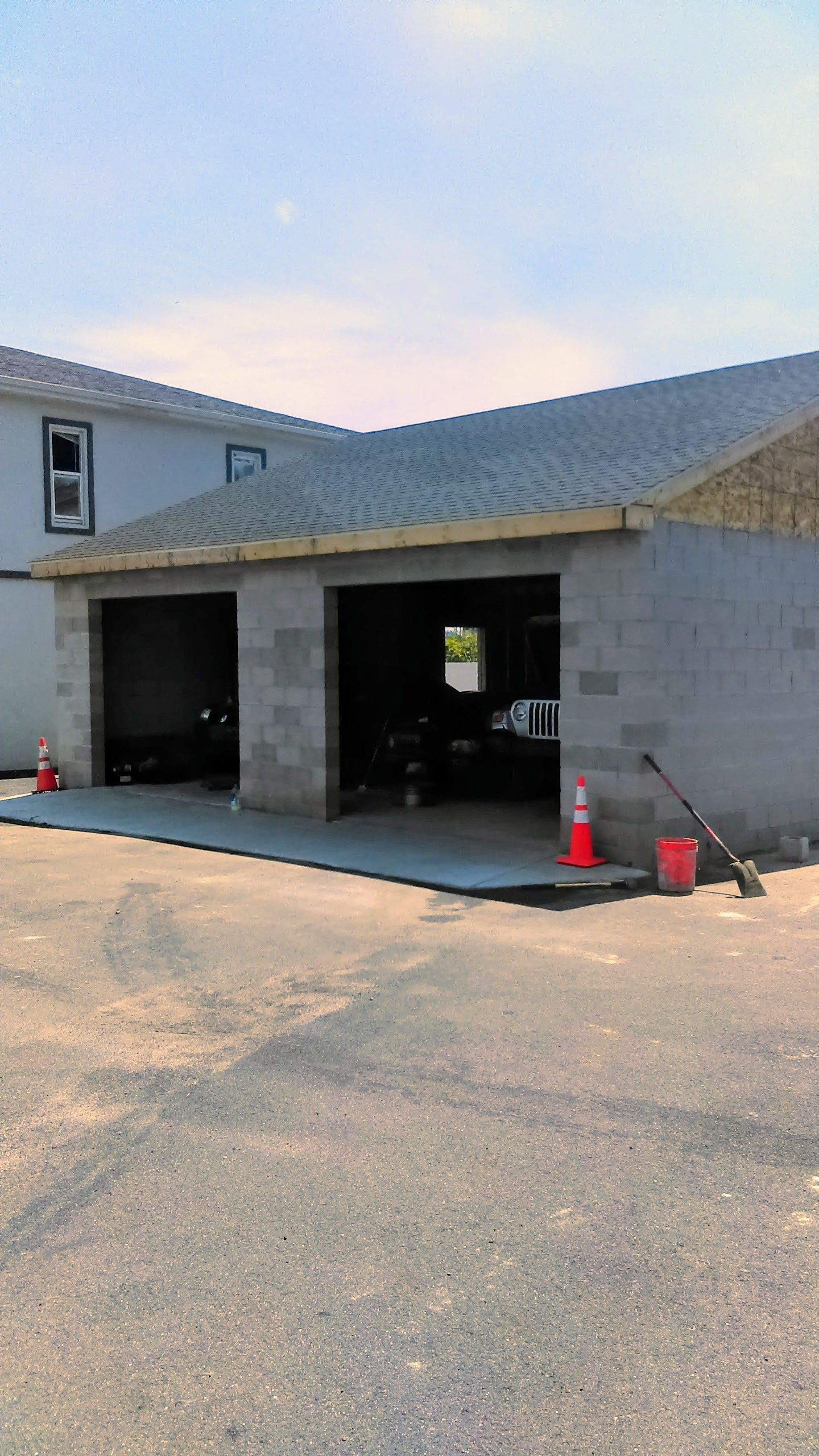 Two-bay cinder block garage under construction, with open bays, adjacent to a light-colored building.