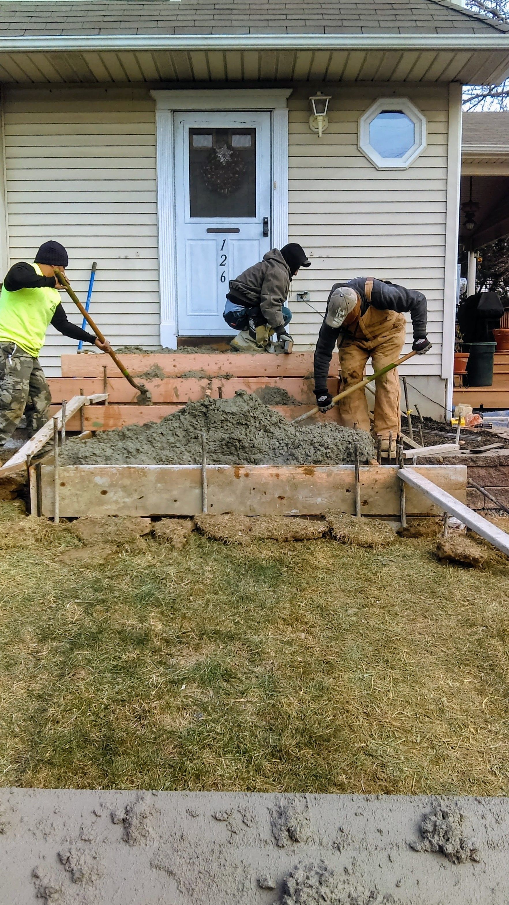 Three workers pouring concrete into forms for front steps.