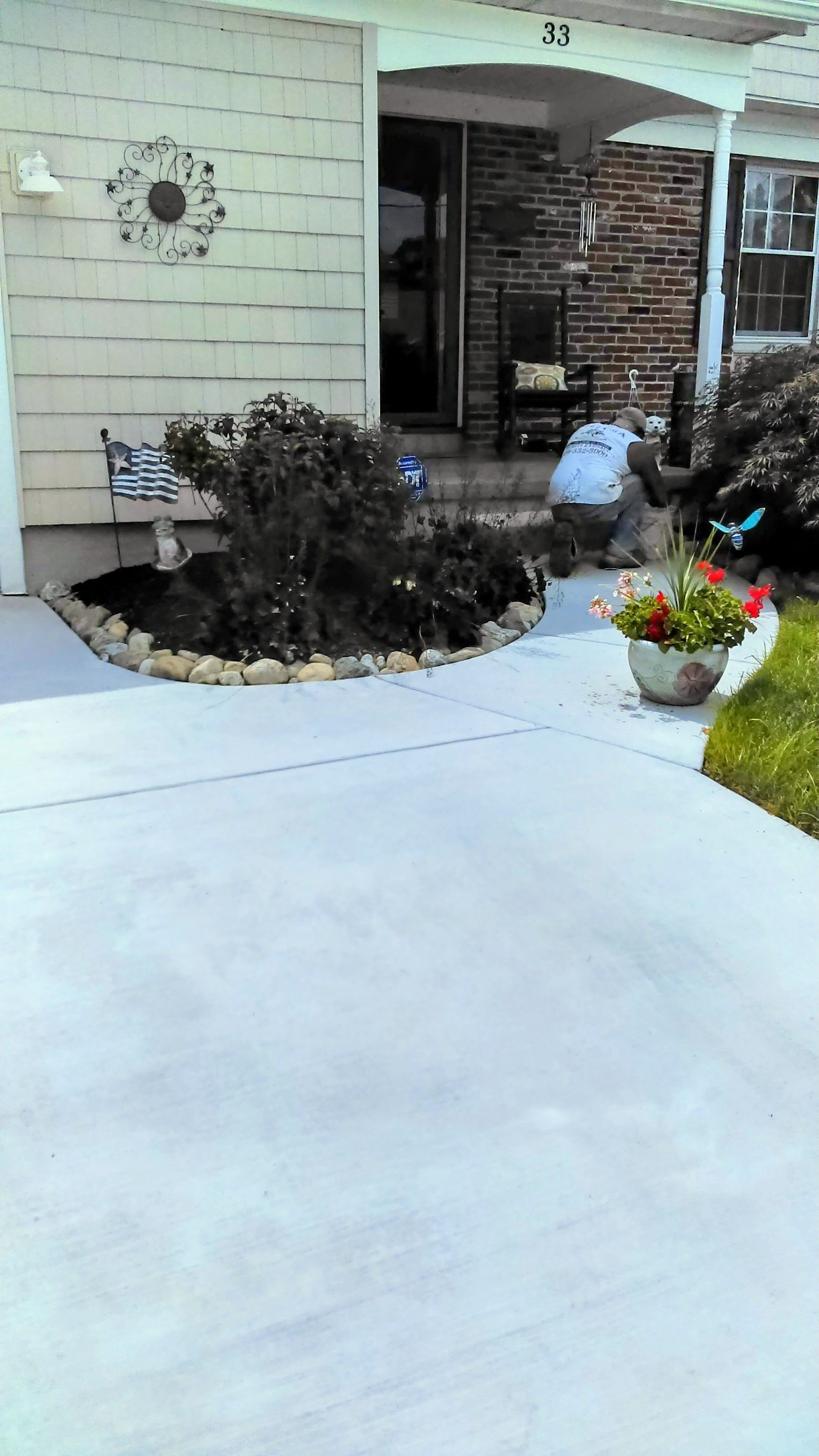 Person gardening near a house with a newly poured concrete driveway and flowerbeds.