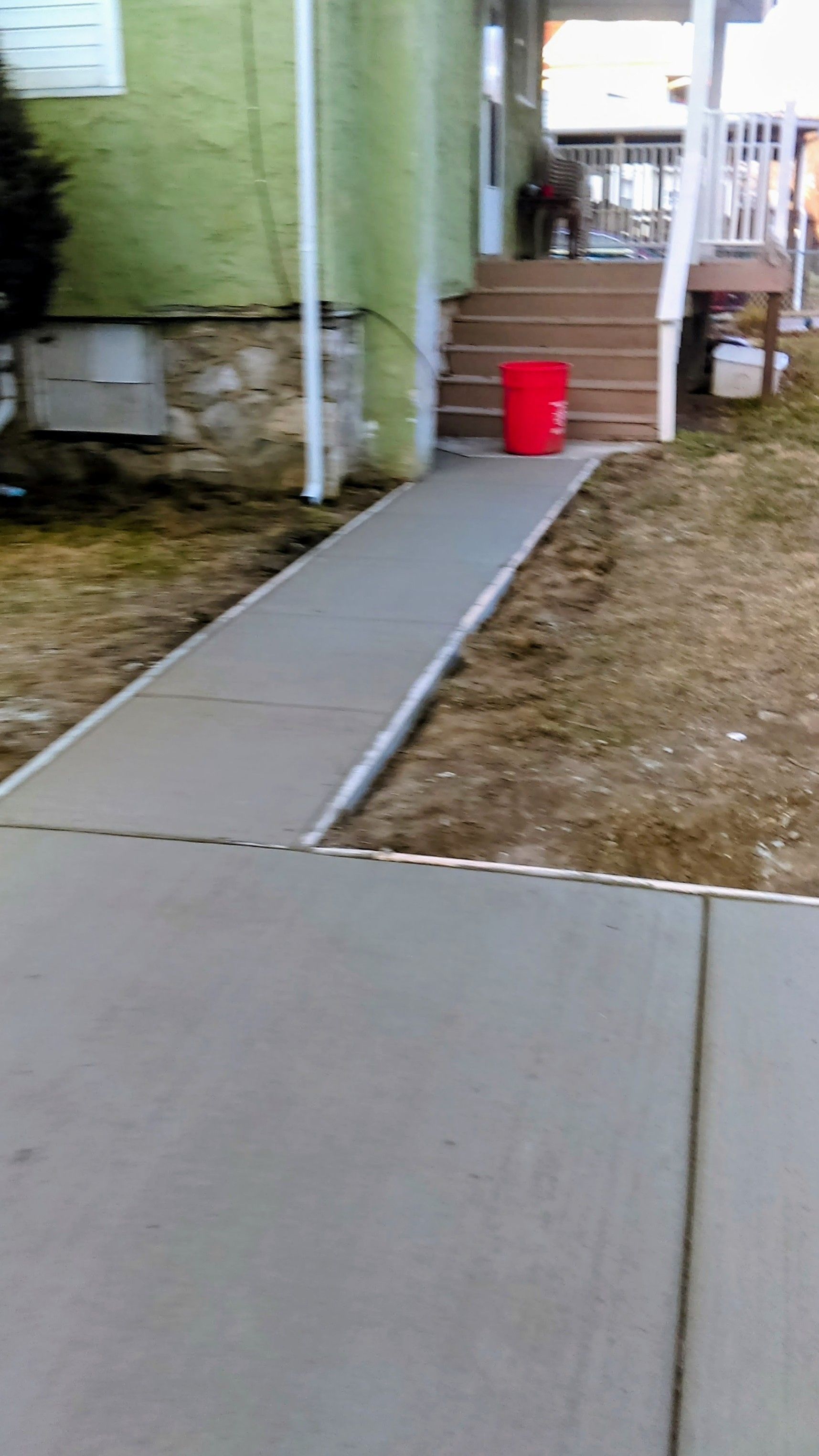 New concrete sidewalk leading to the steps of a house with a red bucket.