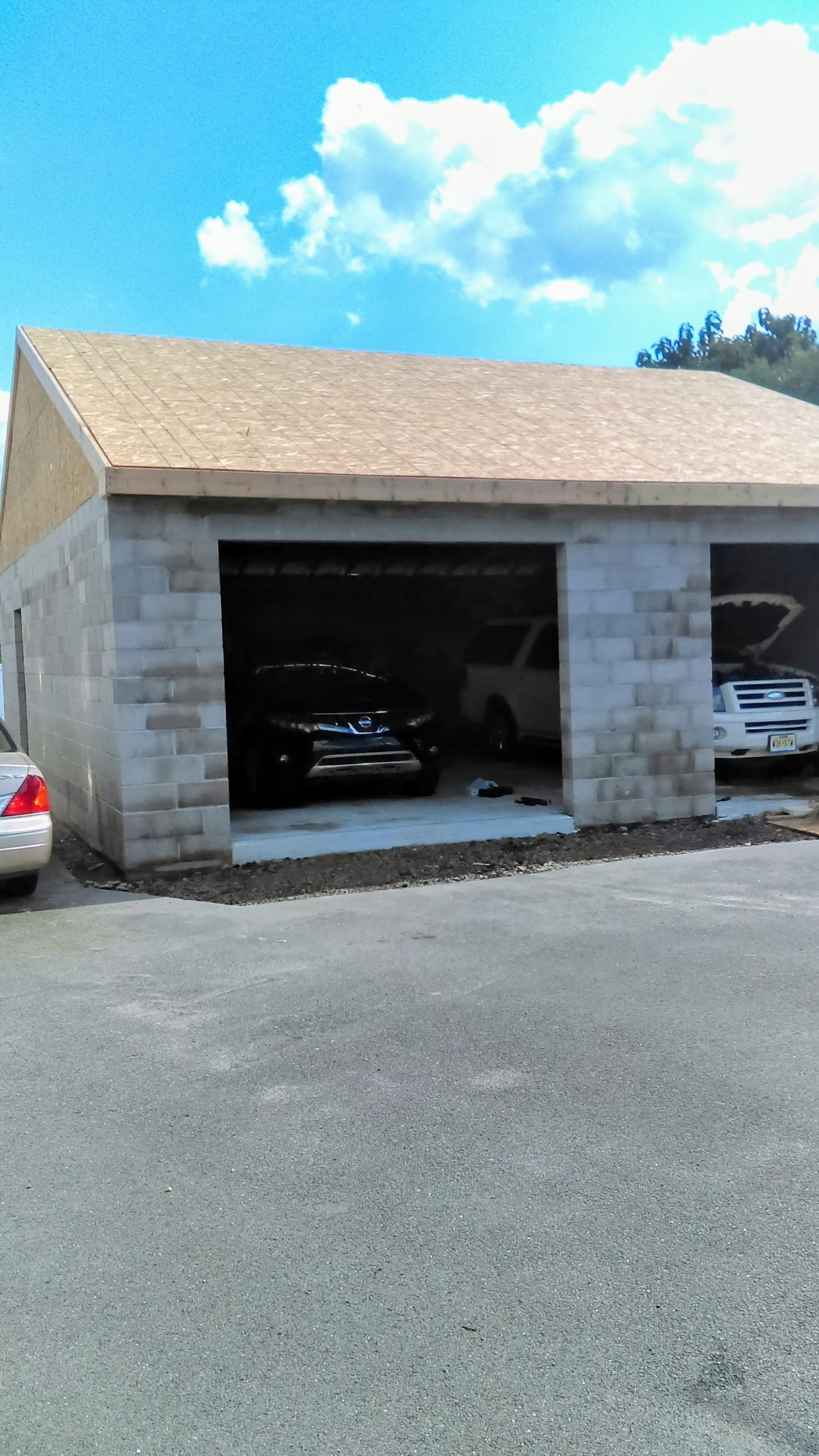 Garage made of gray cinder blocks with two bays. Two vehicles are parked inside. Sunny day with blue sky.