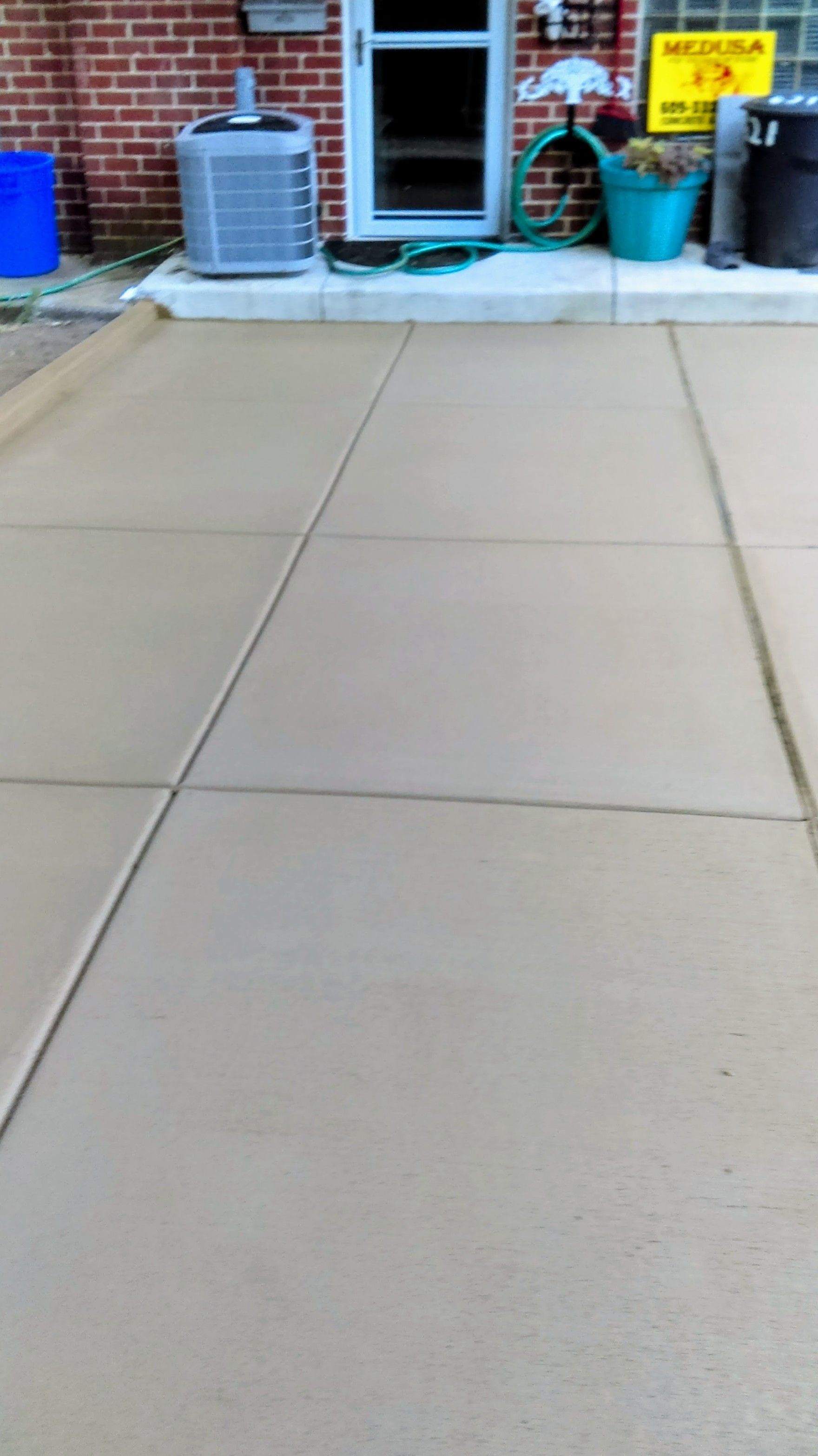 Tan concrete driveway with expansion joints in front of a brick building.