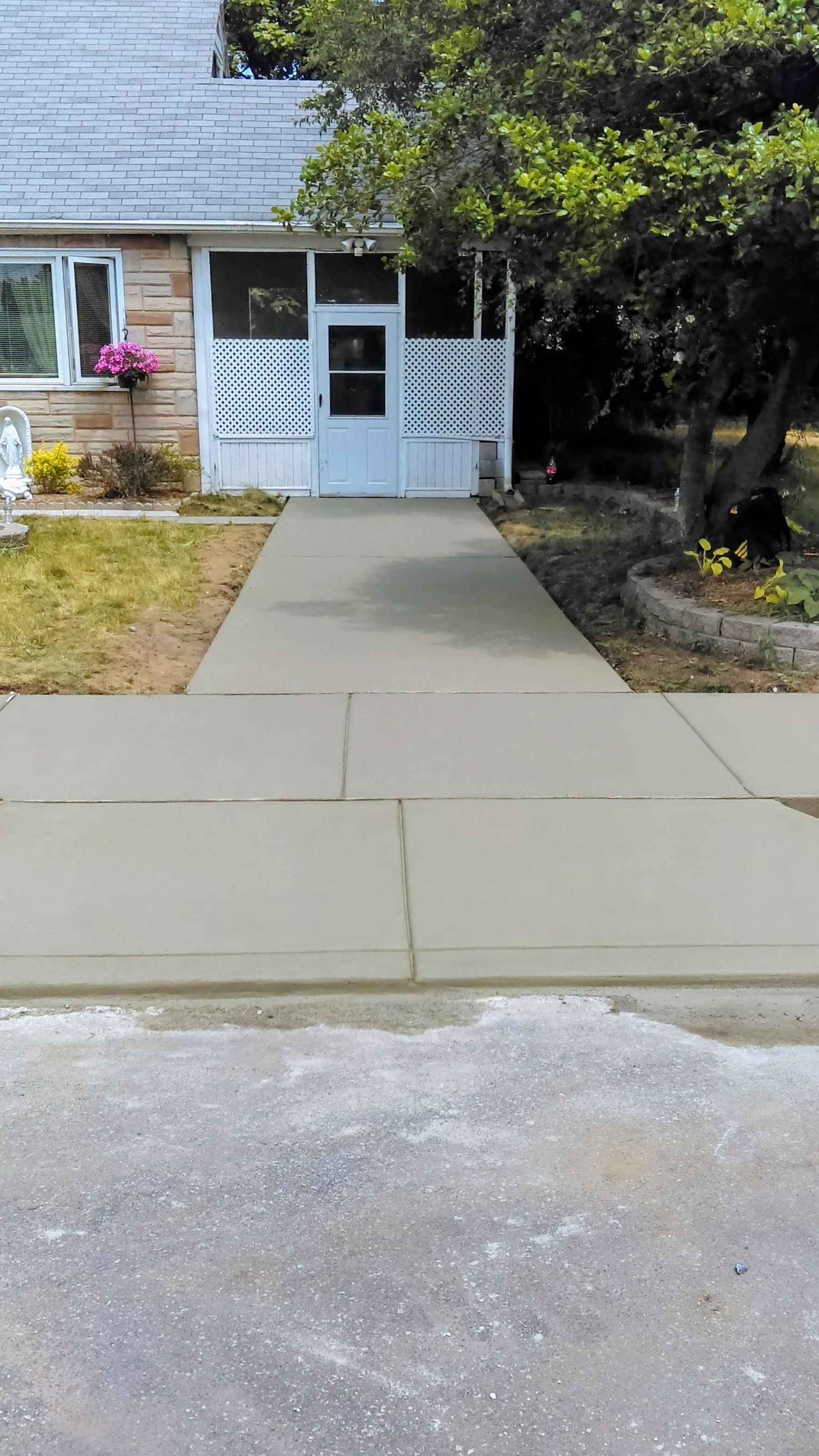 Concrete walkway leading to a light blue door of a house with a screen porch, tree to the right.