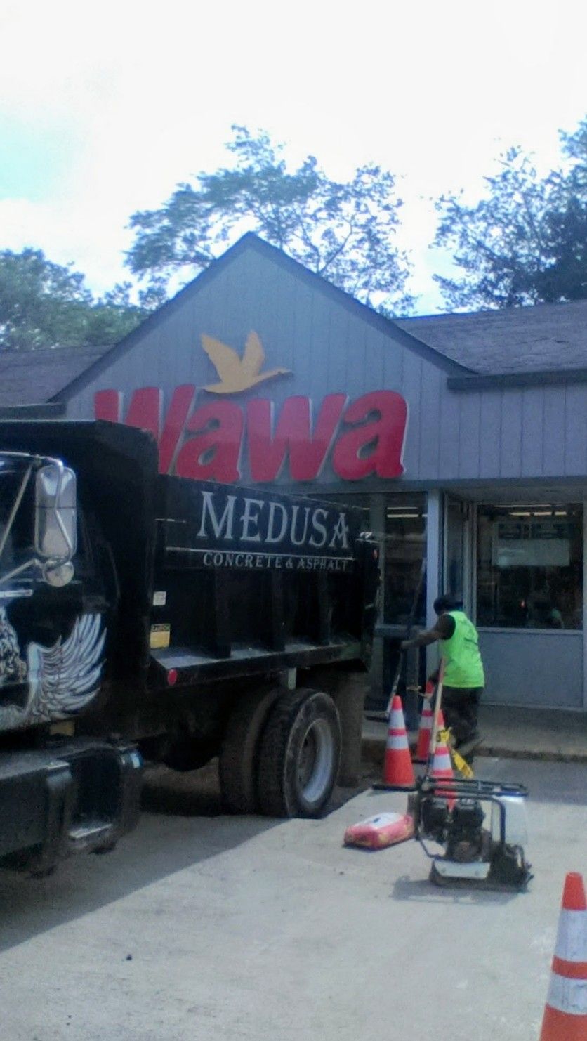 Dump truck parked in front of a Wawa store, construction cones and a worker in a safety vest present.