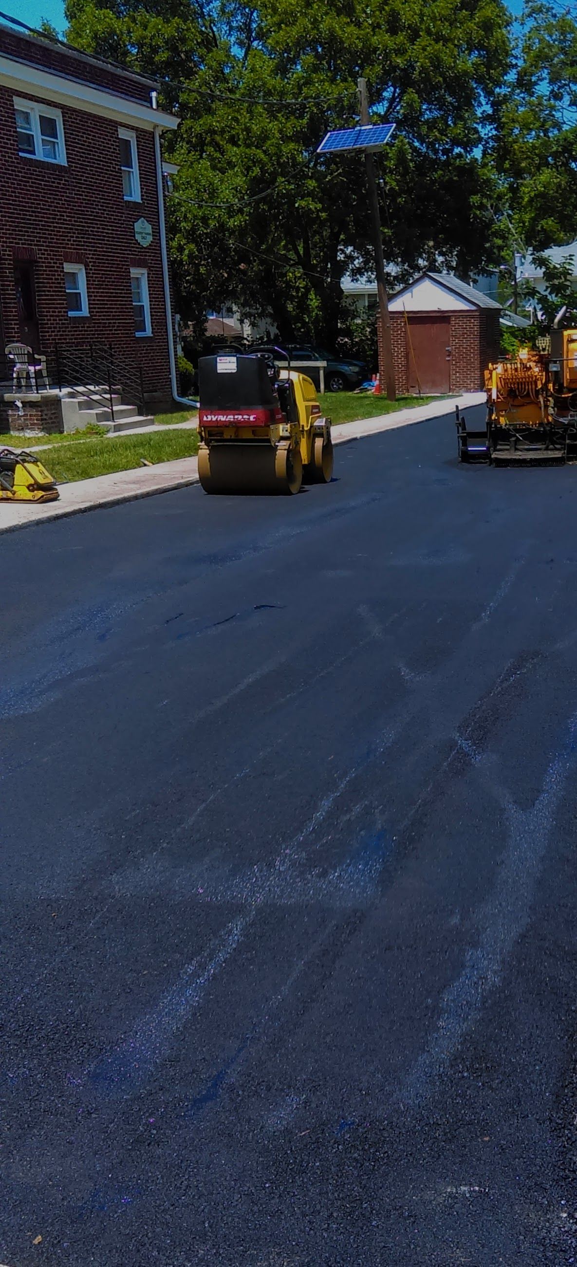 Asphalt paving on a residential street; construction workers using machinery.