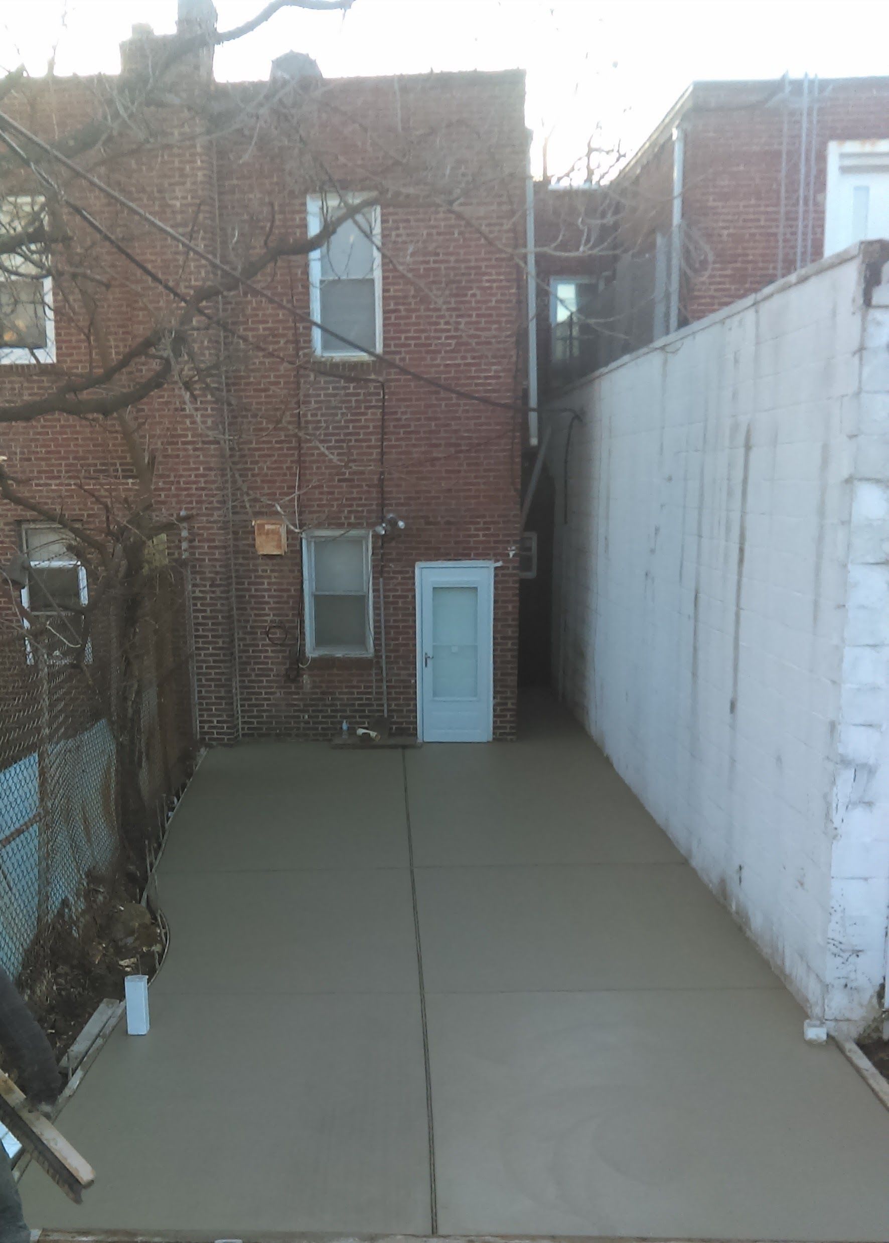 Backyard with a light gray concrete patio, brick building, and a white side wall.