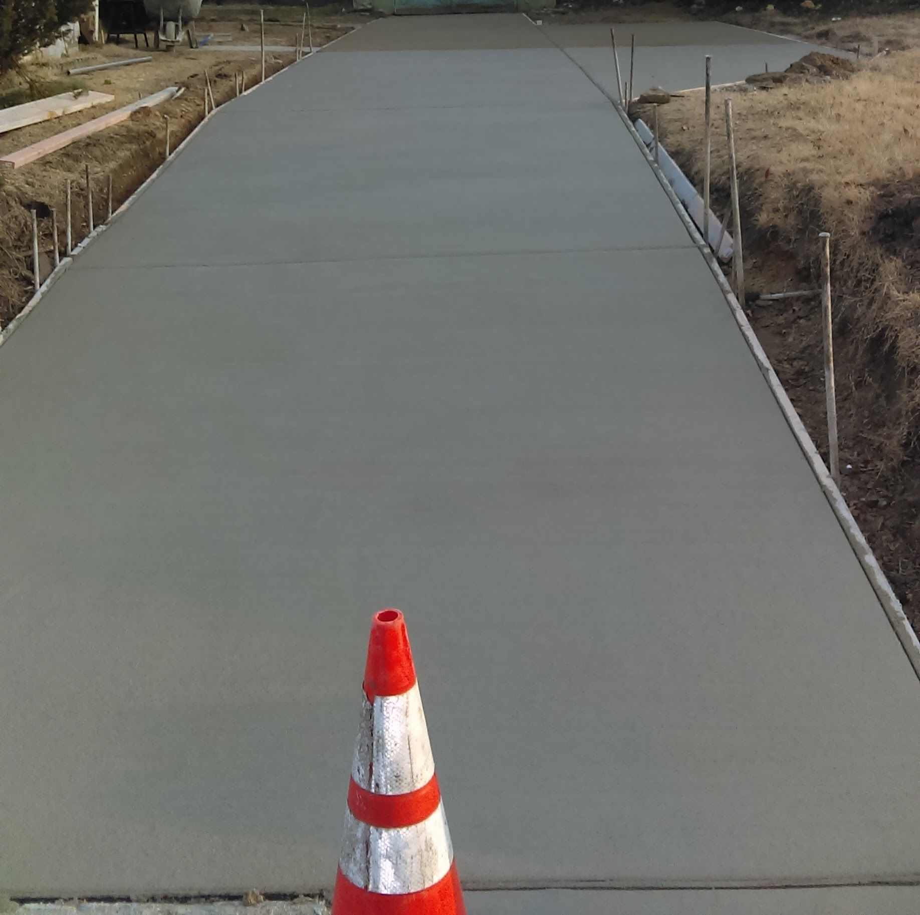 Newly poured concrete driveway with a safety cone in front.