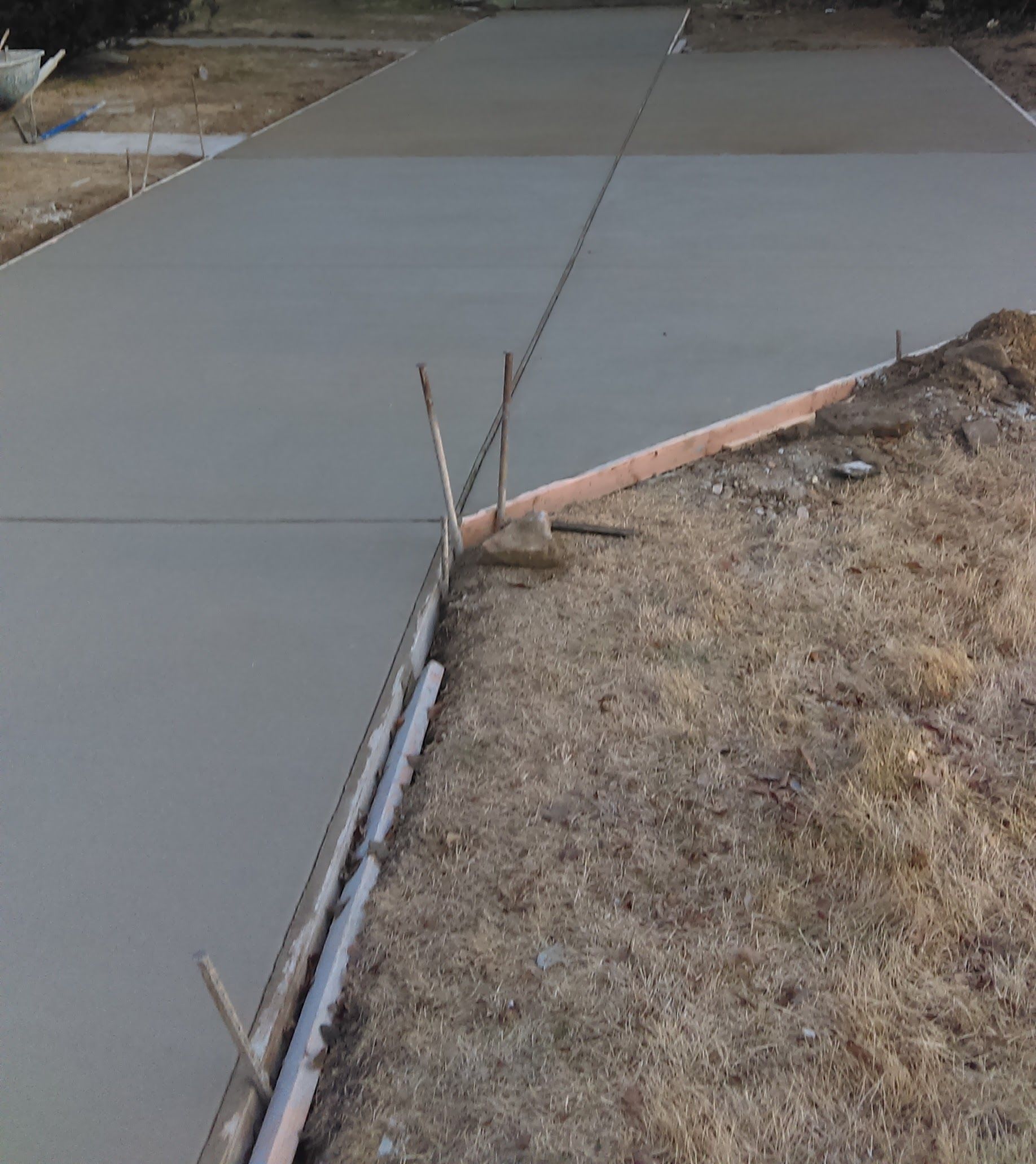 Freshly poured concrete driveway, bordered by wooden forms and dry grass.
