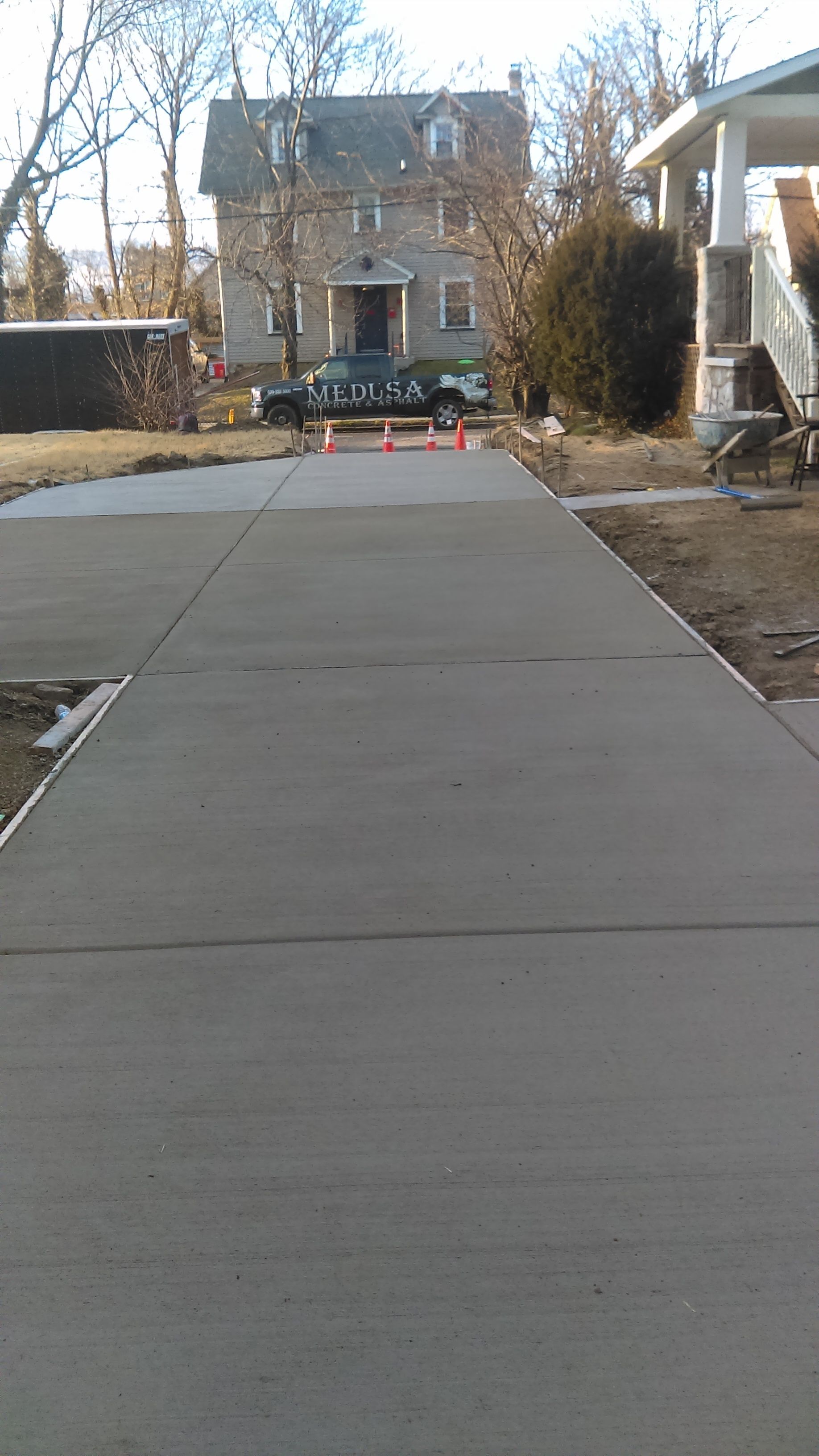 Newly poured concrete driveway with orange cones leading to a gray house.