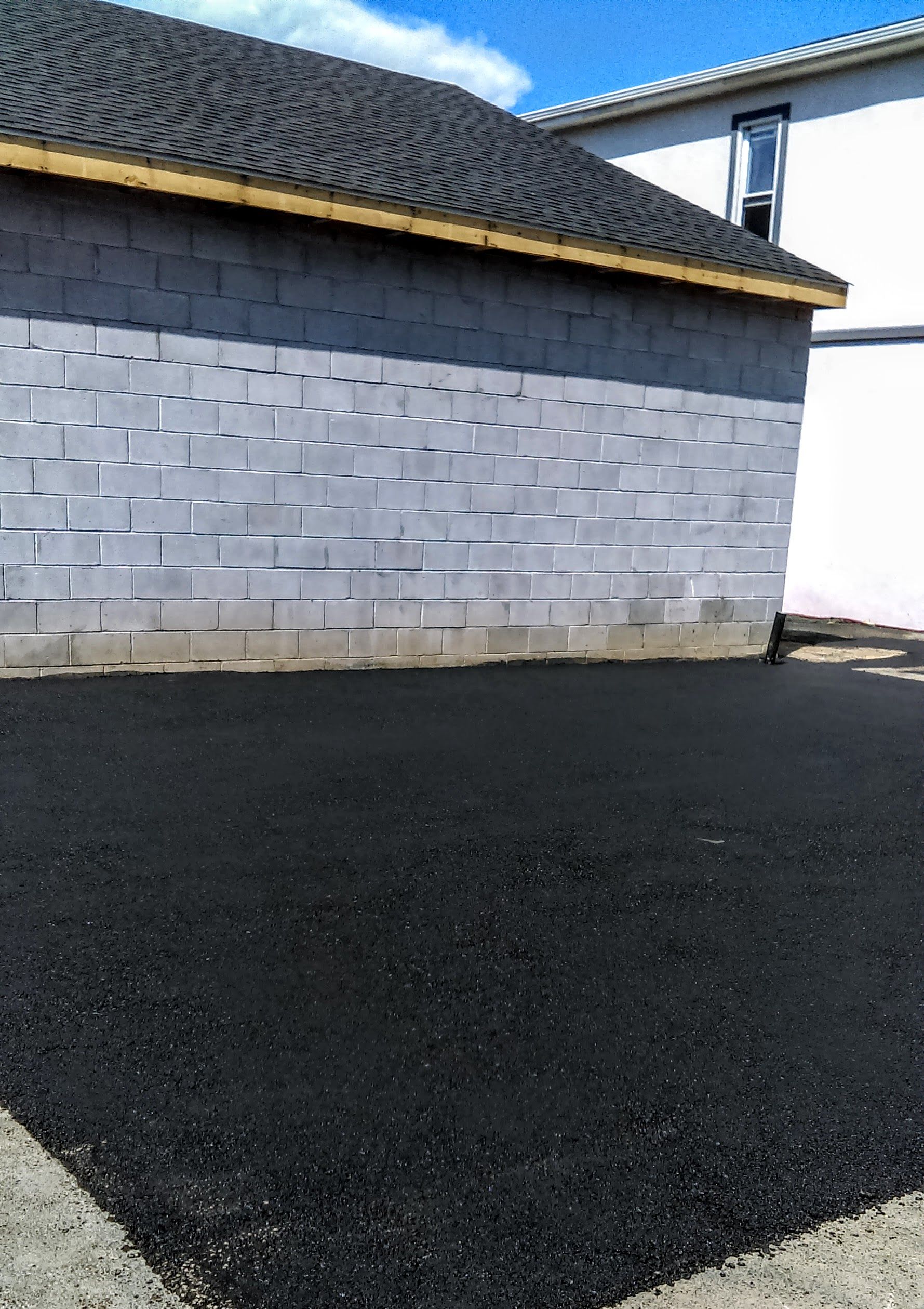 Asphalt paving in front of a gray cinder block building with a dark roof.