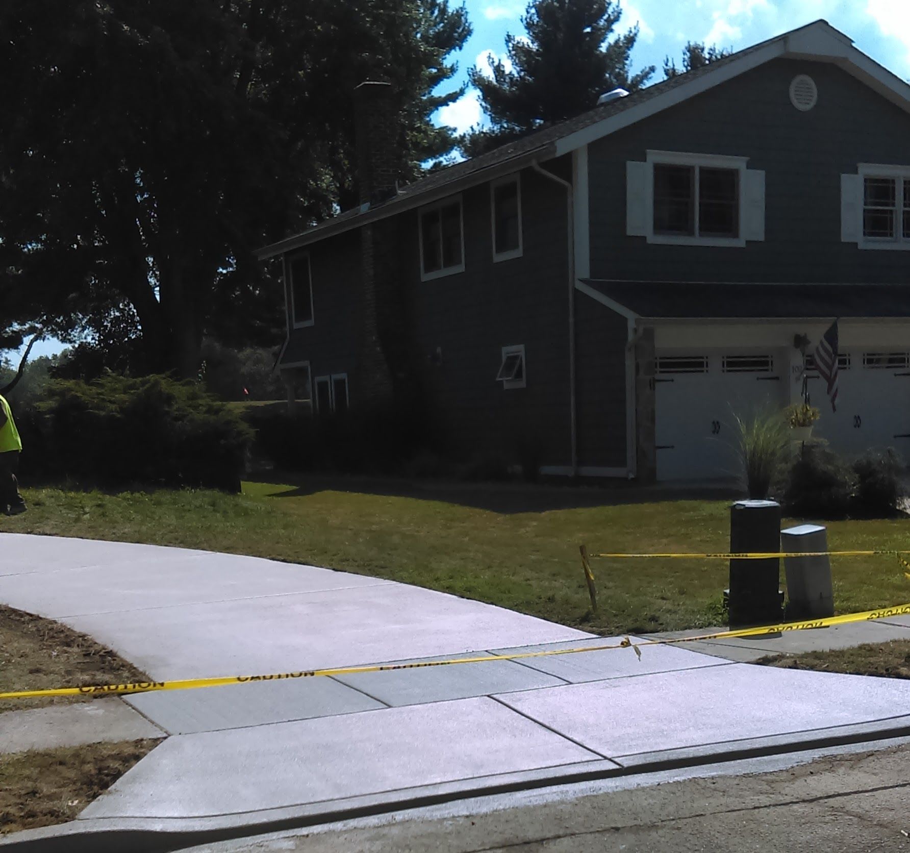 New concrete driveway in front of a two-story house, caution tape, lawn, sunny day.