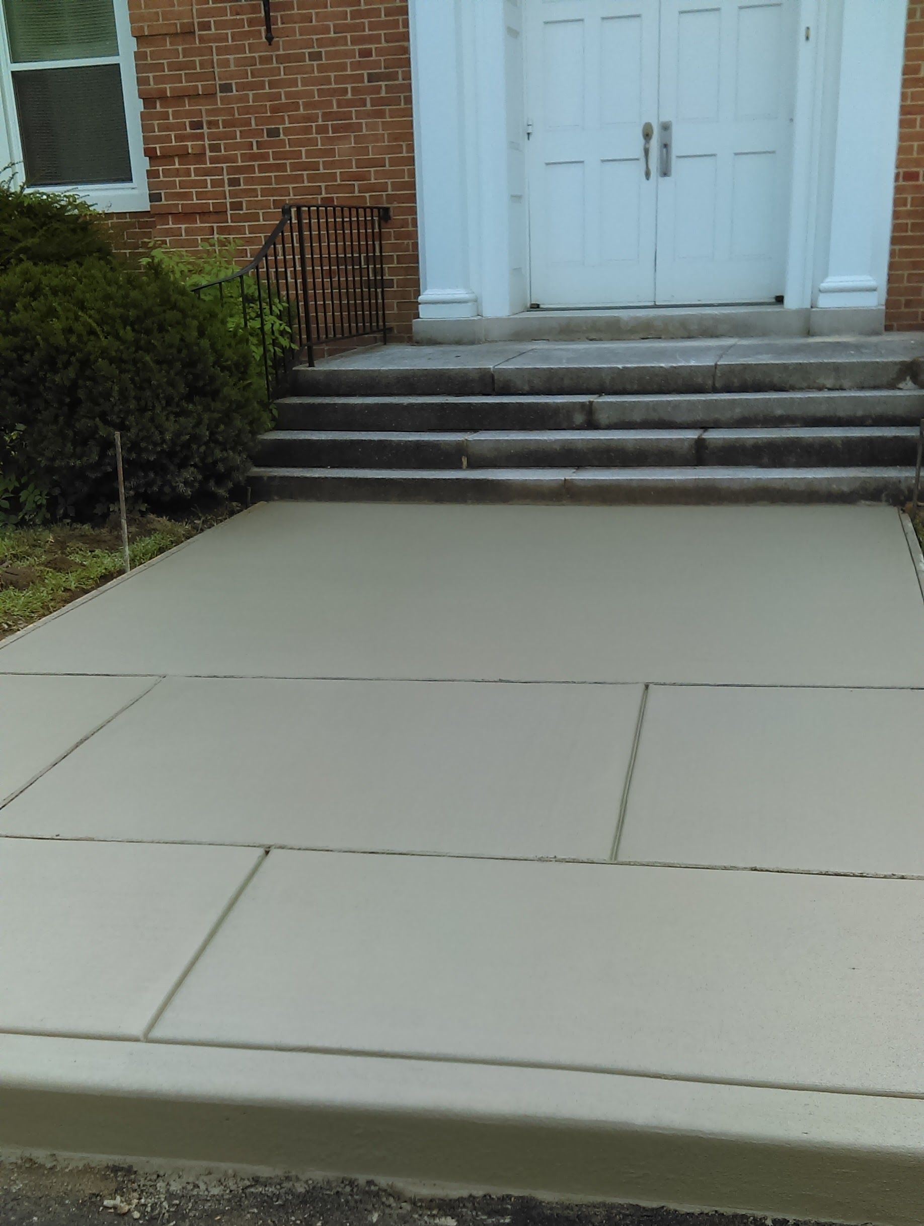 Gray concrete sidewalk leading to the entrance of a brick building with white doors.