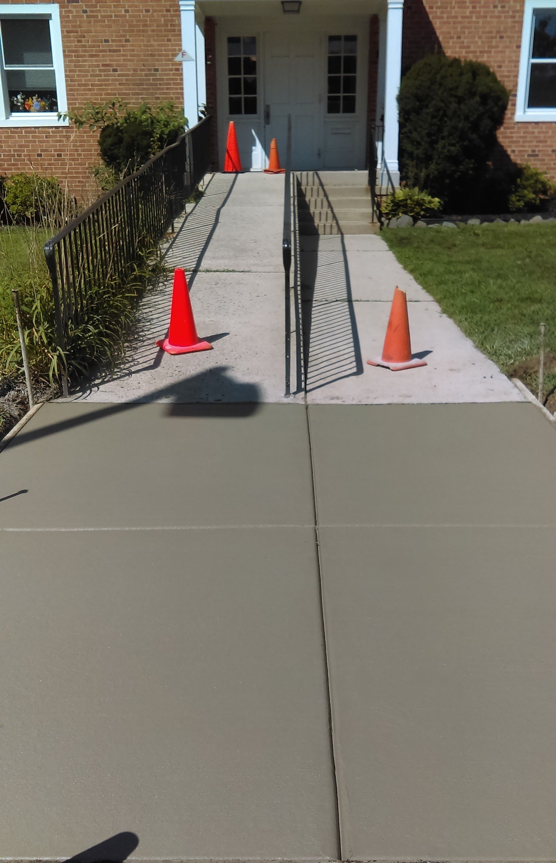 Freshly poured concrete sidewalk with ramp leading to a building entrance; safety cones are in place.