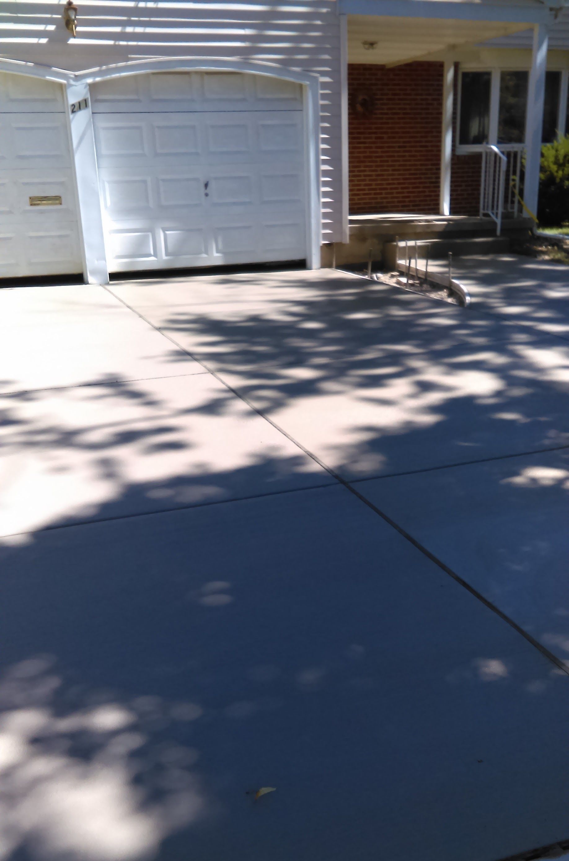 White garage door, driveway, and house front with brick and a small set of steps.