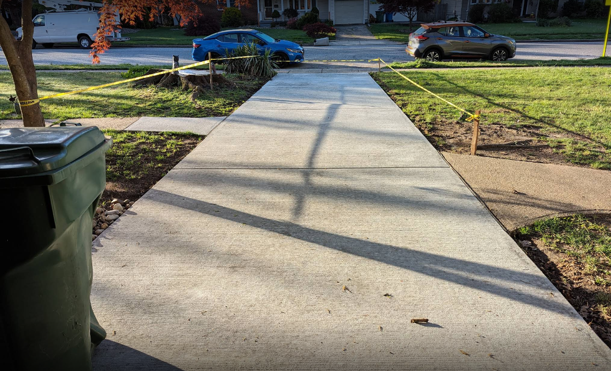 A concrete sidewalk with a blue car parked on the side of it.